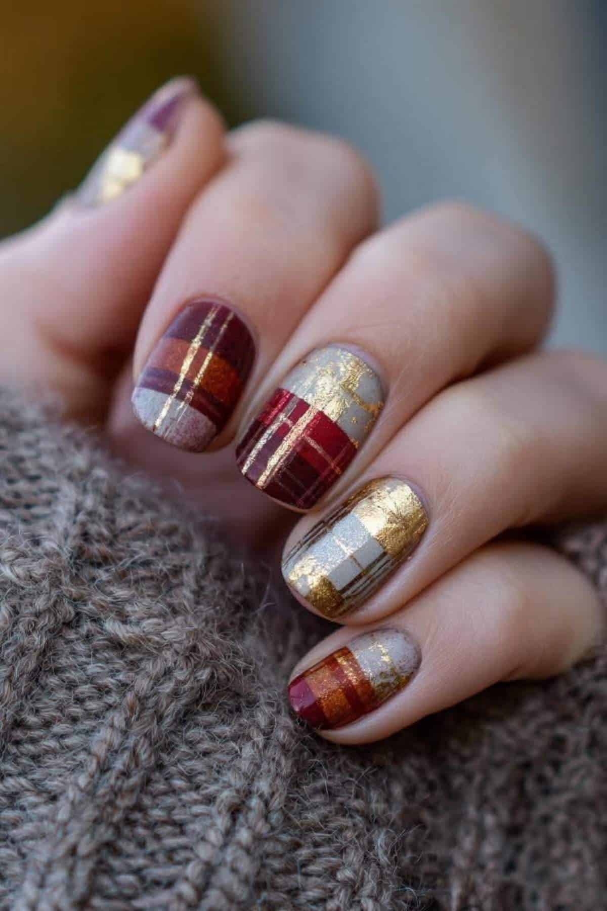 A hand with manicured nails featuring a plaid pattern in shades of red, gold, gray, and white, holding a knitted fabric.