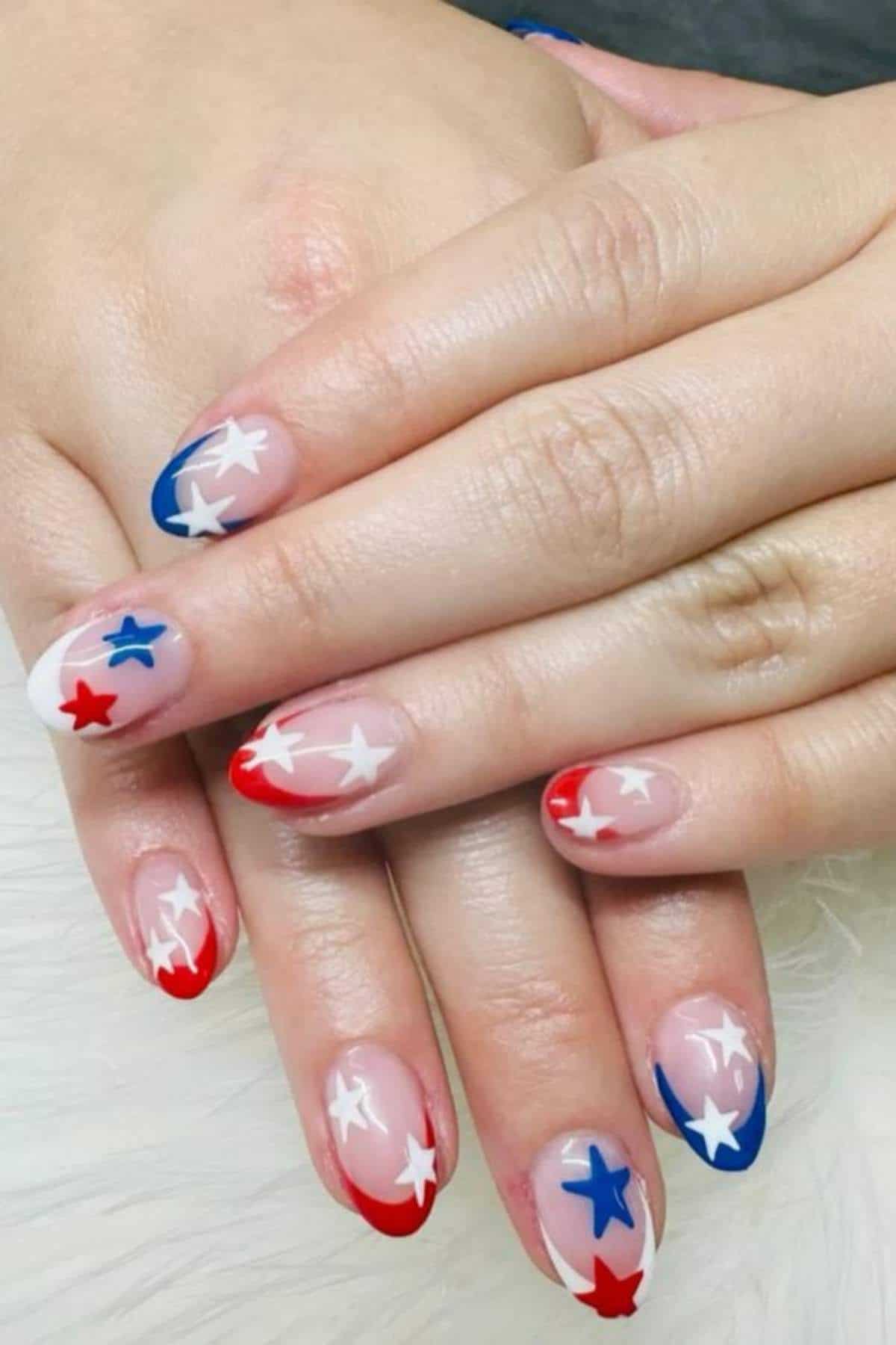 Hands with almond-shaped nails painted in red, white, and blue tips with white and blue star designs on each nail.
