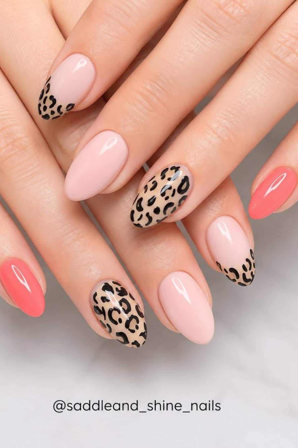 Hands with almond-shaped nails featuring a mix of solid pink, coral, and nude polish, plus accent nails with a black and brown leopard print design.