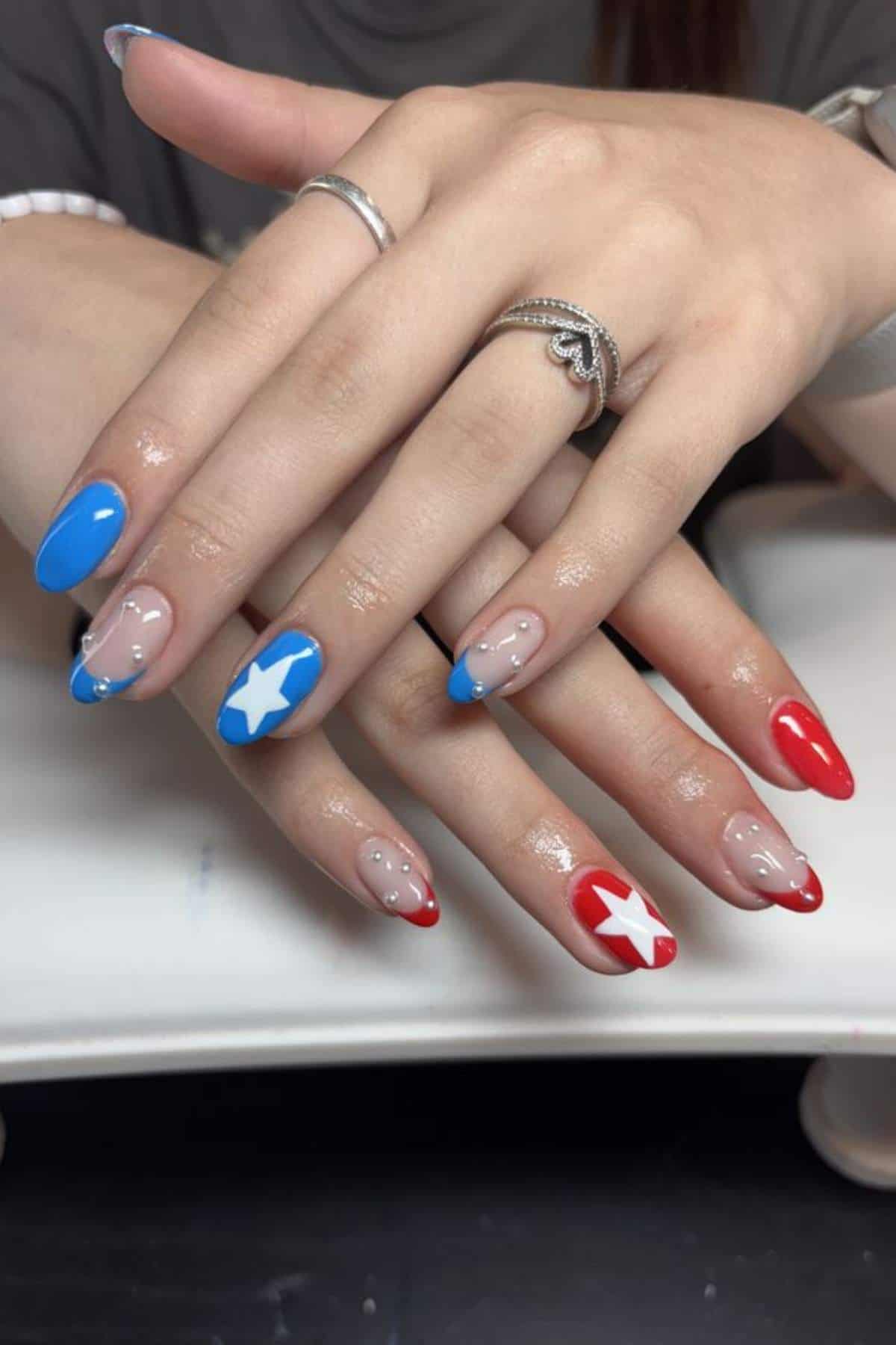 Hands with manicured nails featuring red and blue tips, some with white star designs, and clear sections showing natural nails.