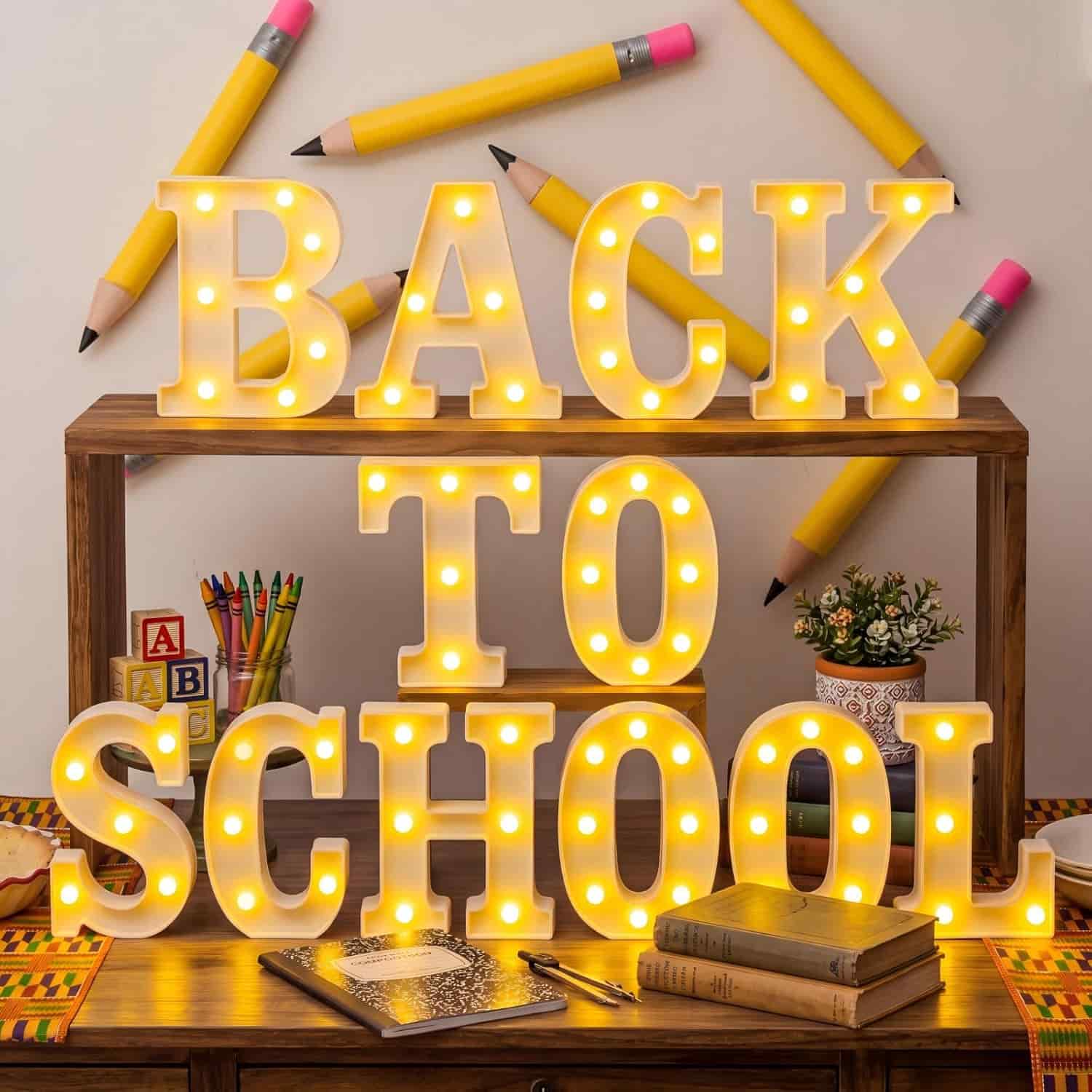 Large illuminated letters spell "BACK TO SCHOOL" on a wooden desk, surrounded by books, pencils, alphabet blocks, and small plants.