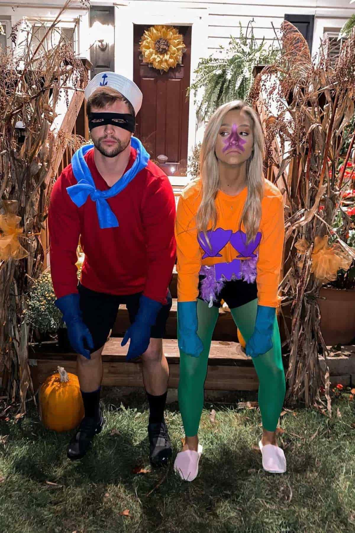 Two people in cartoon-inspired costumes pose outside; the man wears a red shirt, blue scarf, sailor hat, and gloves, while the woman wears a purple shell bra, orange shirt, green tights, and purple shorts.