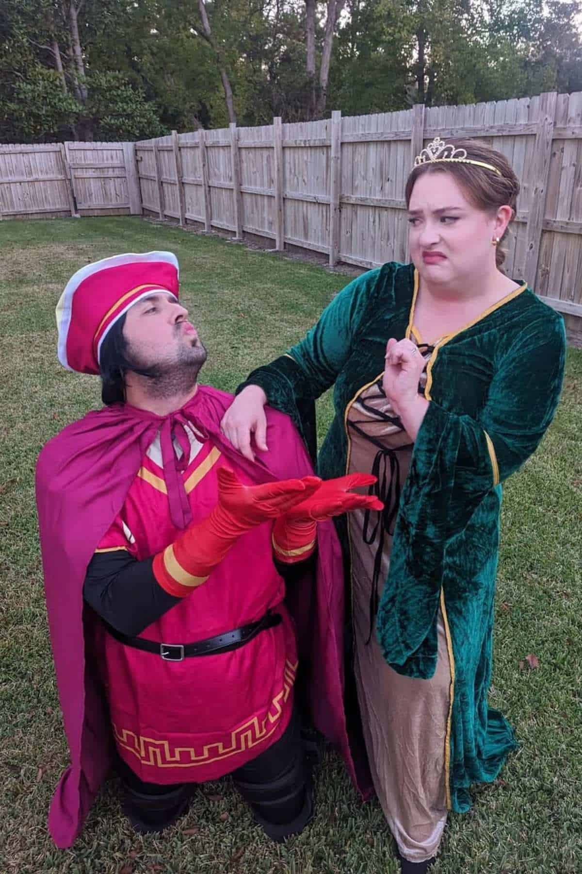 Two adults in costumes are outdoors; one dressed as a prince is kneeling and proposing, while the other, dressed as a princess, looks away with a displeased expression.