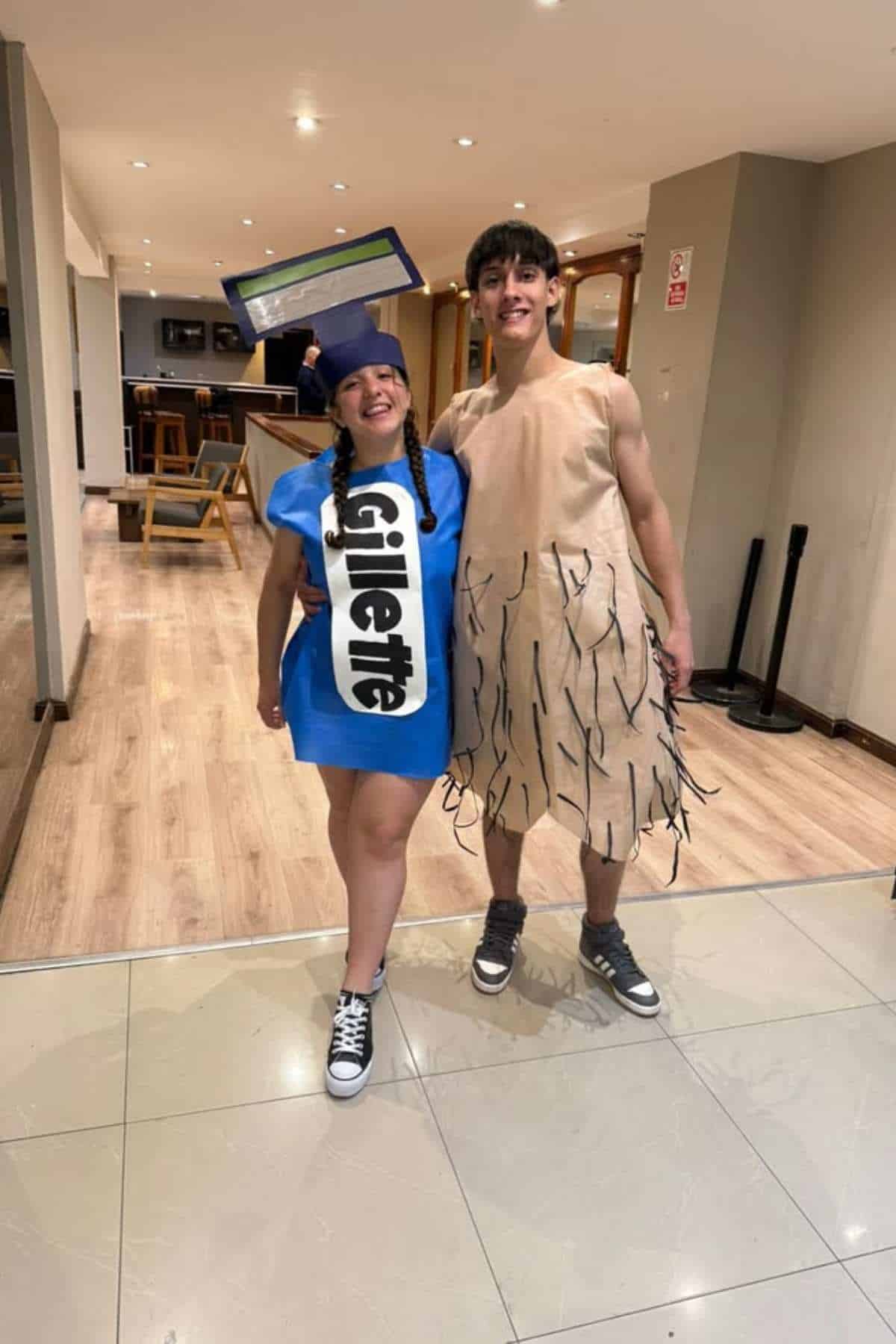 Two people in costumes: one dressed as a Gillette razor, the other as a hairy leg. They are standing and smiling in a well-lit hallway.