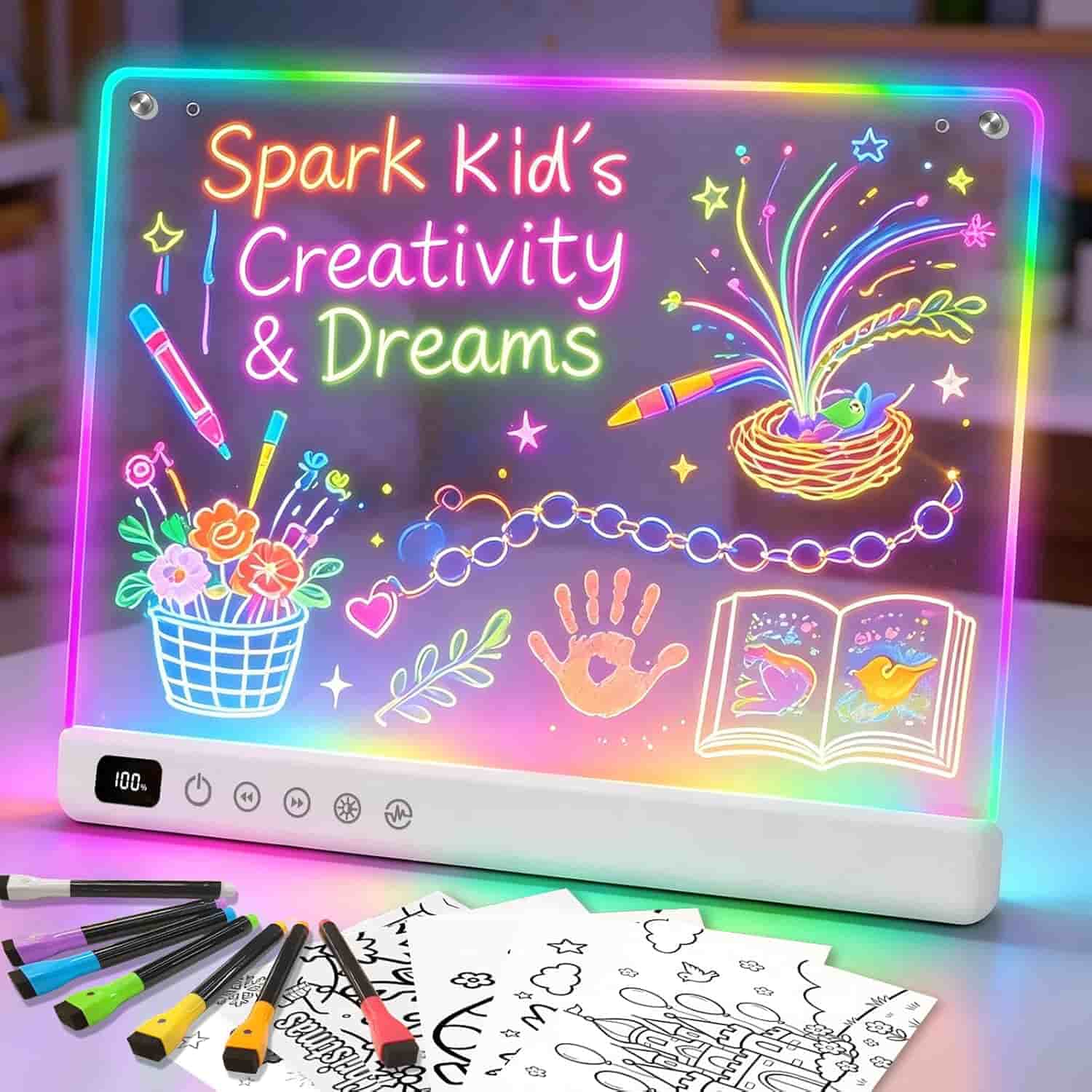 A light-up drawing board displays colorful neon art with the words "Spark Kid's Creativity & Dreams," surrounded by drawings of flowers, a book, and a handprint. Markers and papers are in front.