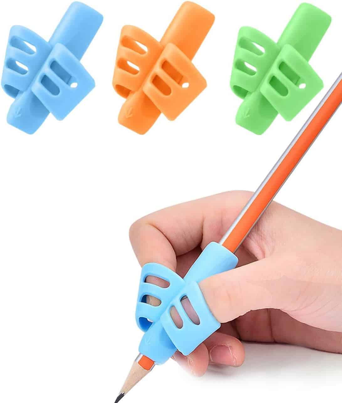 A hand holds a pencil fitted with a blue silicone writing grip; additional orange, green, and blue grips are shown above.