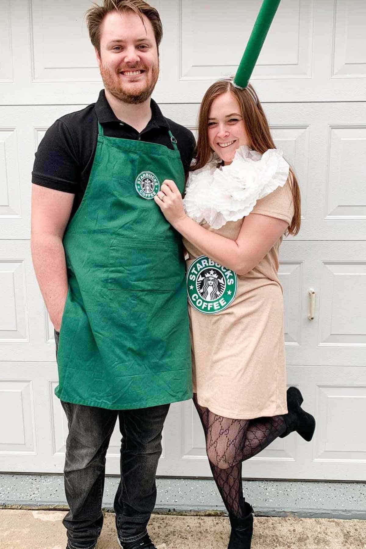 Two people in Starbucks-themed costumes pose in front of a garage door; one wears a green apron, the other has a Starbucks logo and a green straw headband.