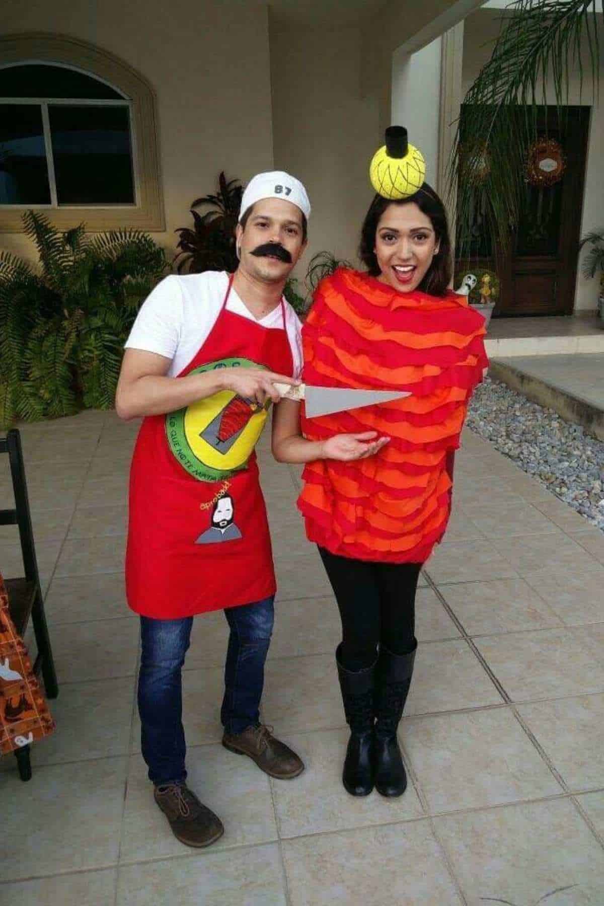 Two people in costumes pose together; one is dressed as a chef with a fake mustache and apron, the other as a red piñata with a small yellow object on their head.