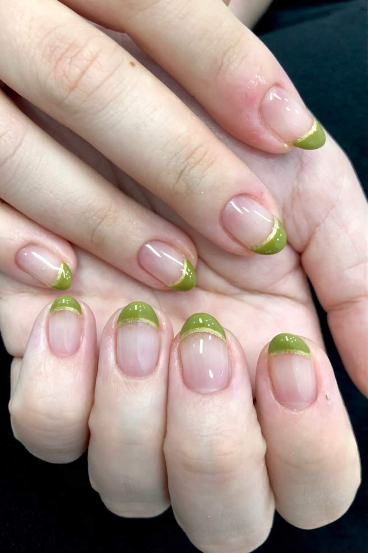 Hands with neatly manicured nails featuring green French tips and a small white dot near each tip, displayed against a dark background.