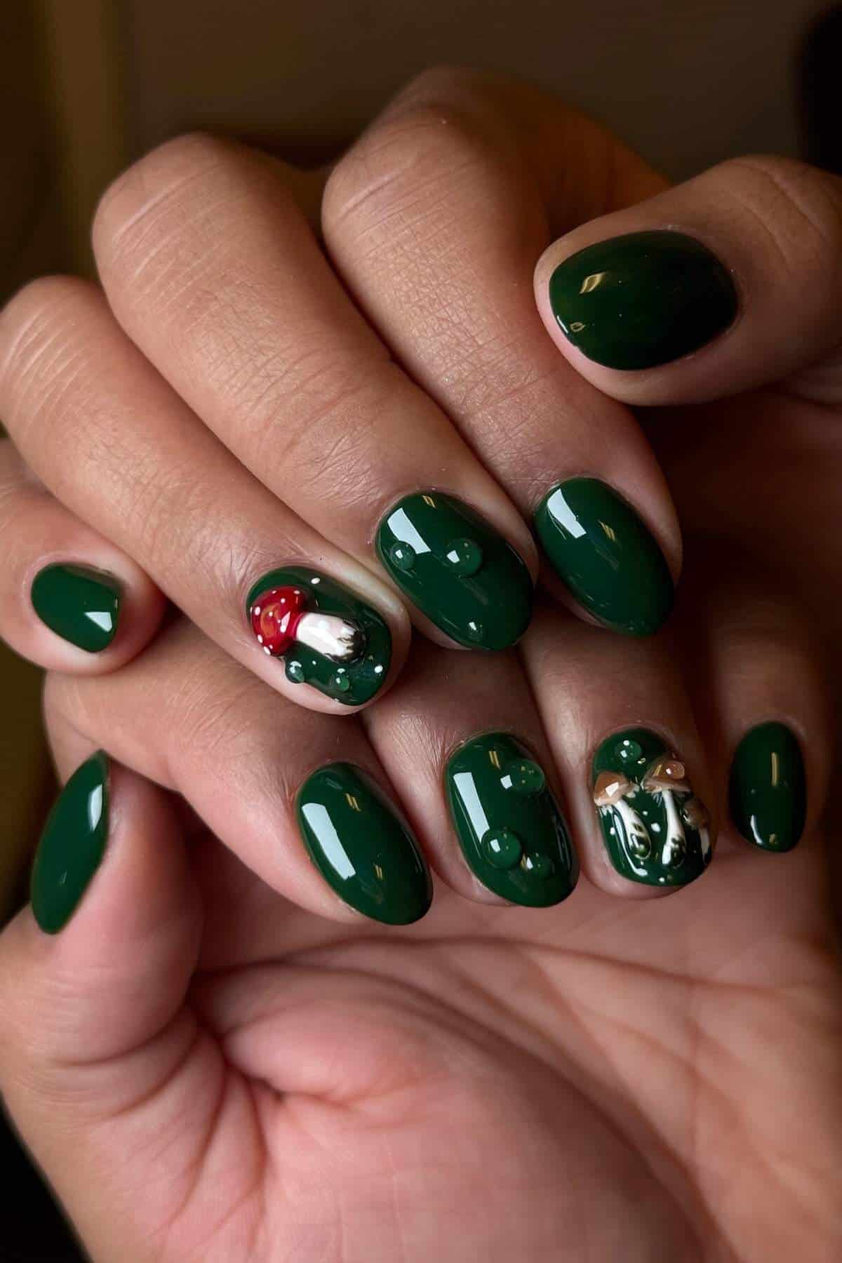 Hands with dark green glossy nail polish; two nails feature detailed mushroom designs with red and white caps and beige stems.