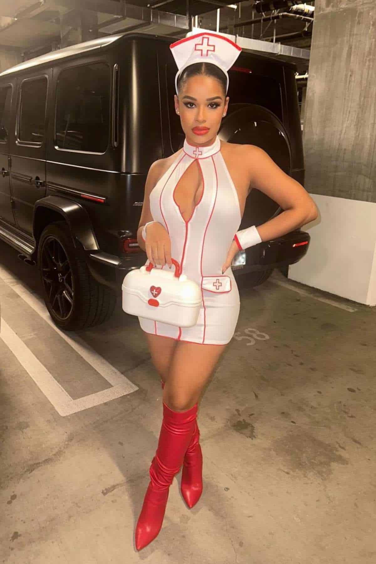 Woman in a nurse costume with red boots and a white nurse hat stands in a parking garage holding a white medical-themed bag.