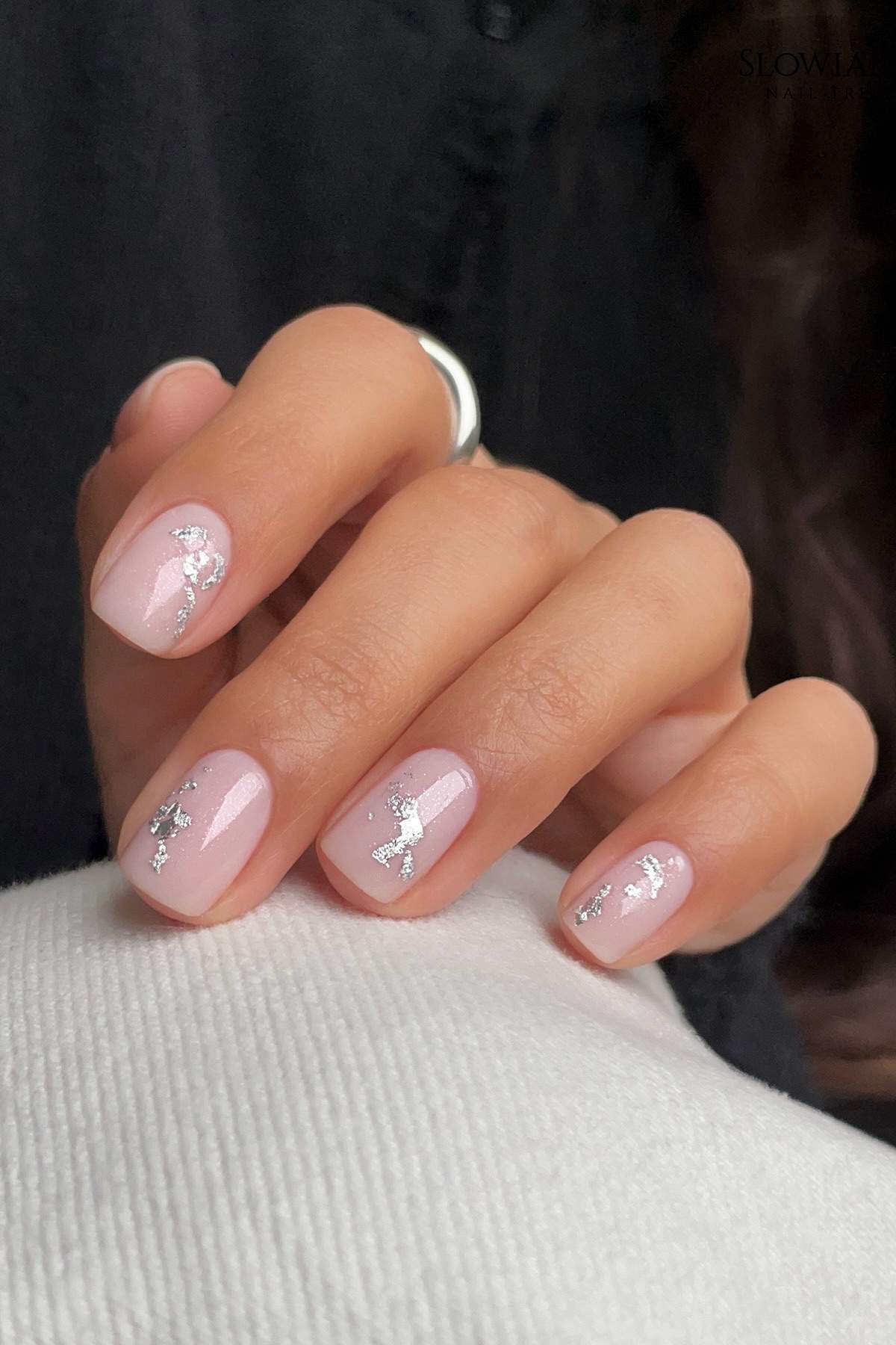 A hand with short, square-shaped nails painted light pink and decorated with silver butterfly nail art.