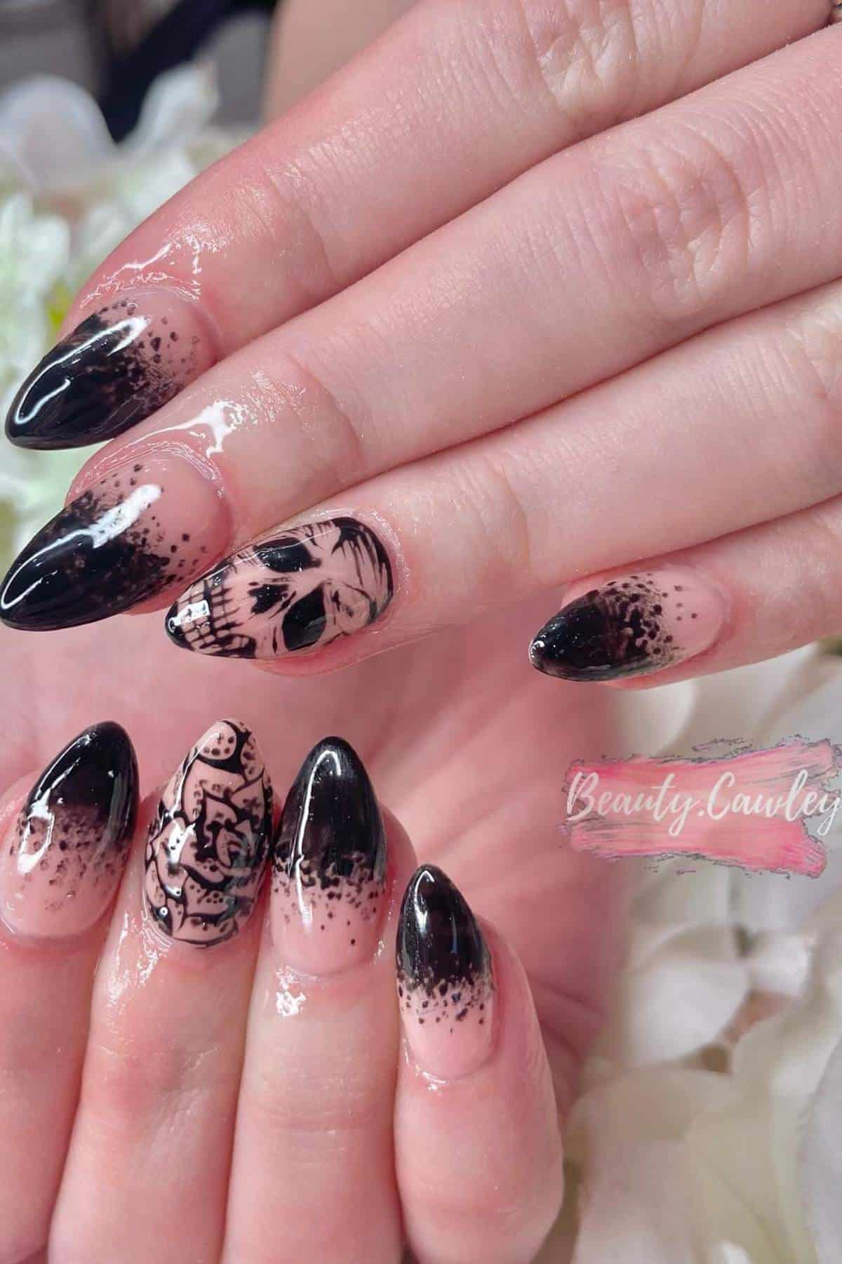Close-up of hands with pointed black and nude gradient nails, some featuring detailed black skull and floral designs on a glossy finish.