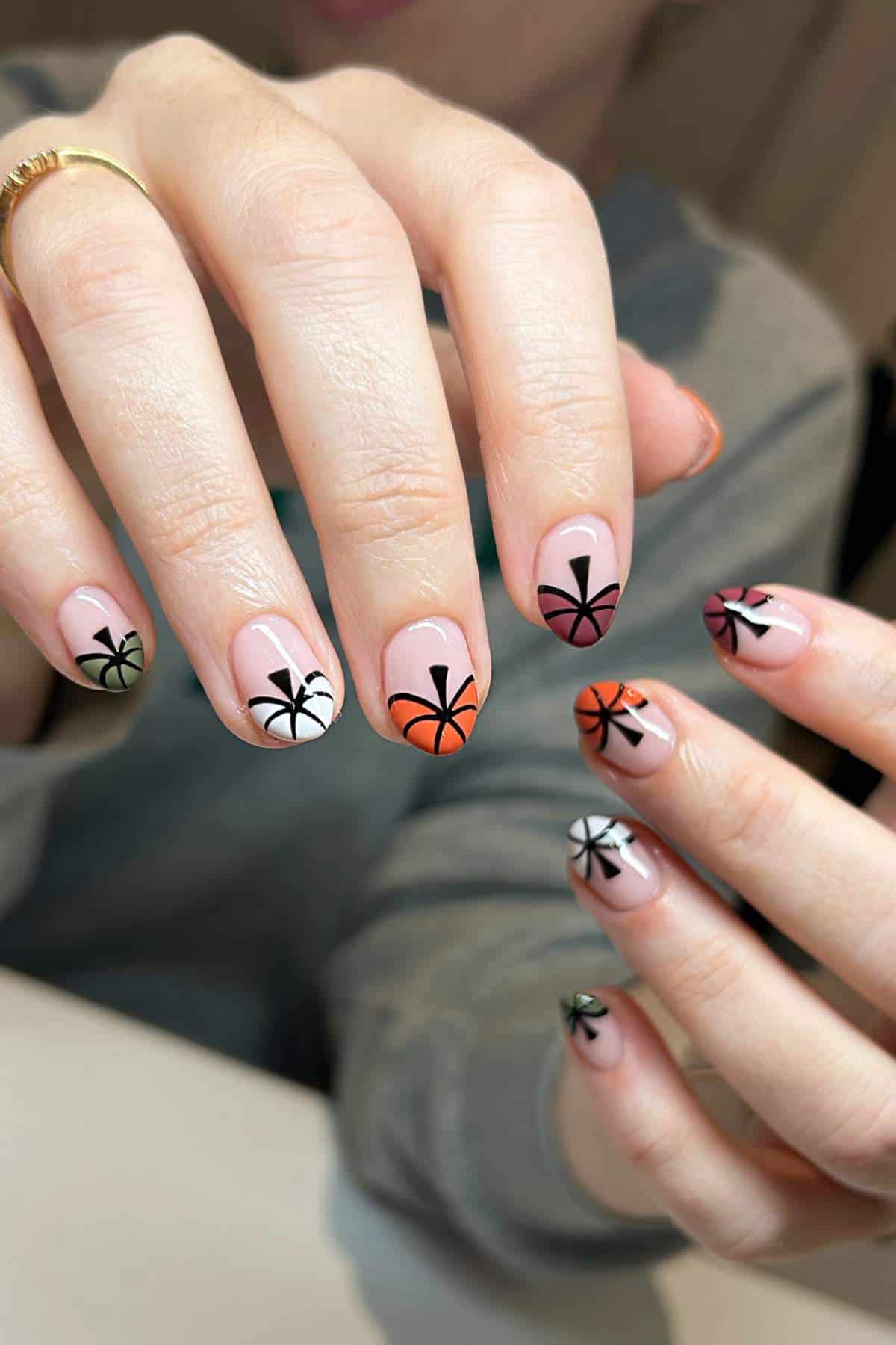 Hands with manicured nails featuring palm tree designs in black, each nail painted with different colored tips including green, white, orange, pink, and maroon.