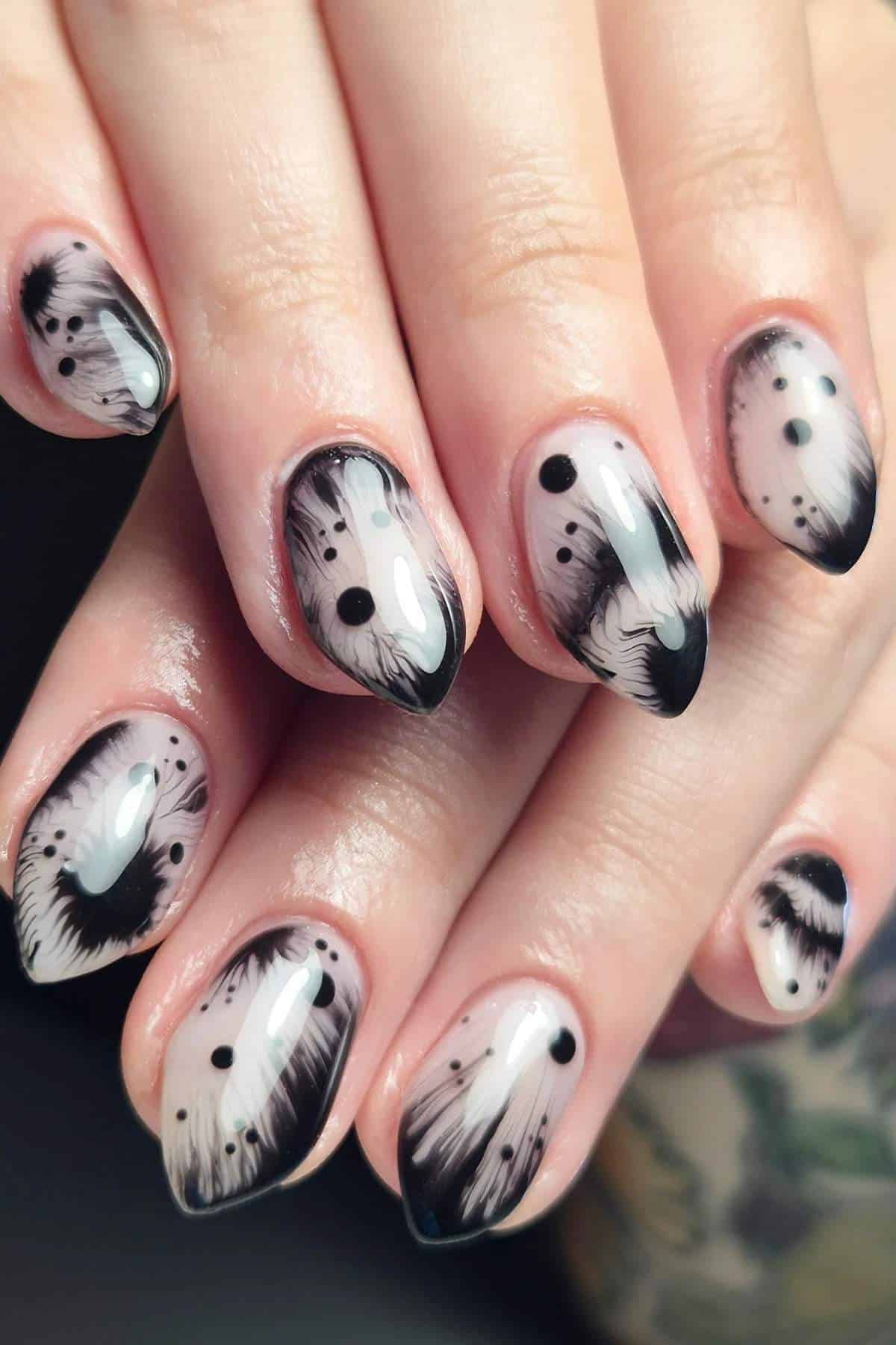 Close-up of hands with almond-shaped nails featuring black abstract feather-like designs and dots on a nude base.