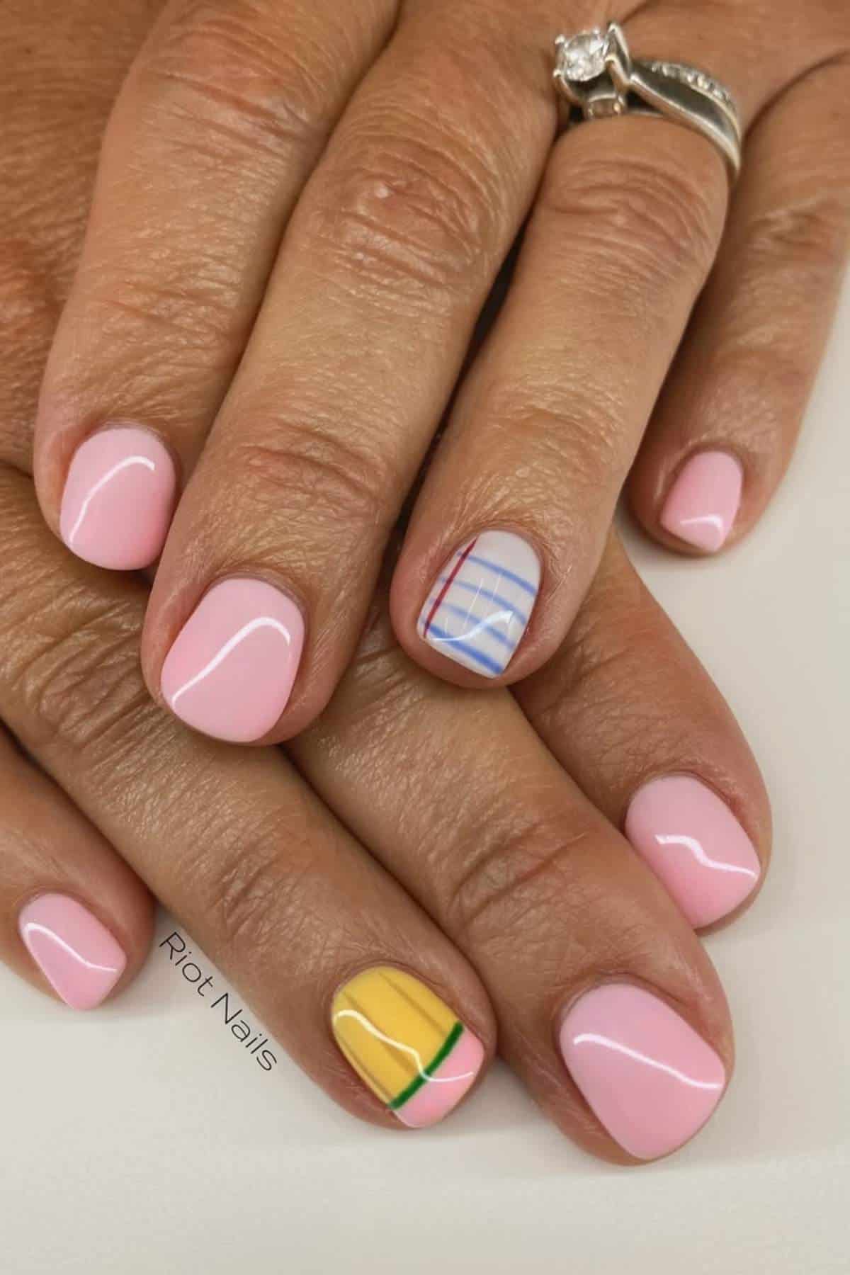 Hands with light pink manicure; the ring fingernail features a notebook paper design and the thumb has a yellow pencil design. A silver ring with a diamond is worn on one finger.