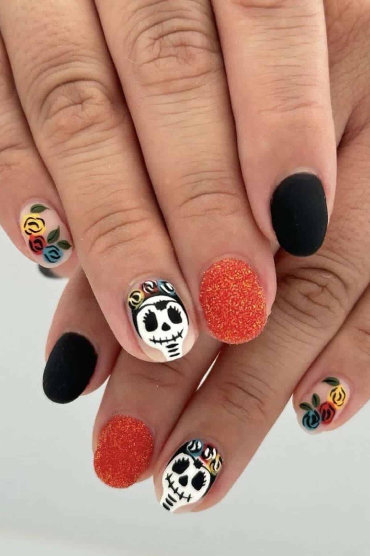 Hands with manicured nails featuring black, orange glitter, skull faces with flower crowns, and colorful rose designs, inspired by Día de los Muertos.