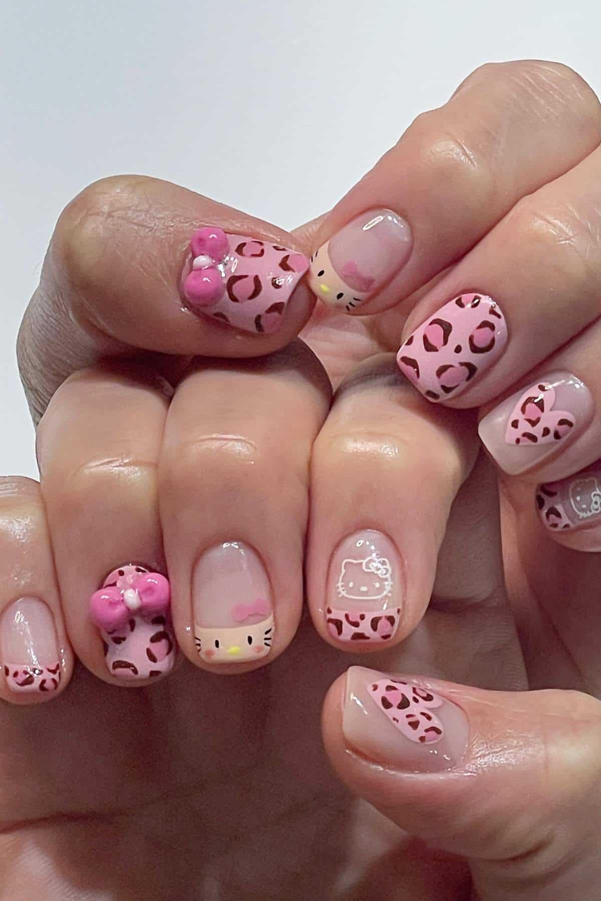 Fingernails with pink leopard print and Hello Kitty designs, including bows, faces, and an outline, on a neutral base.