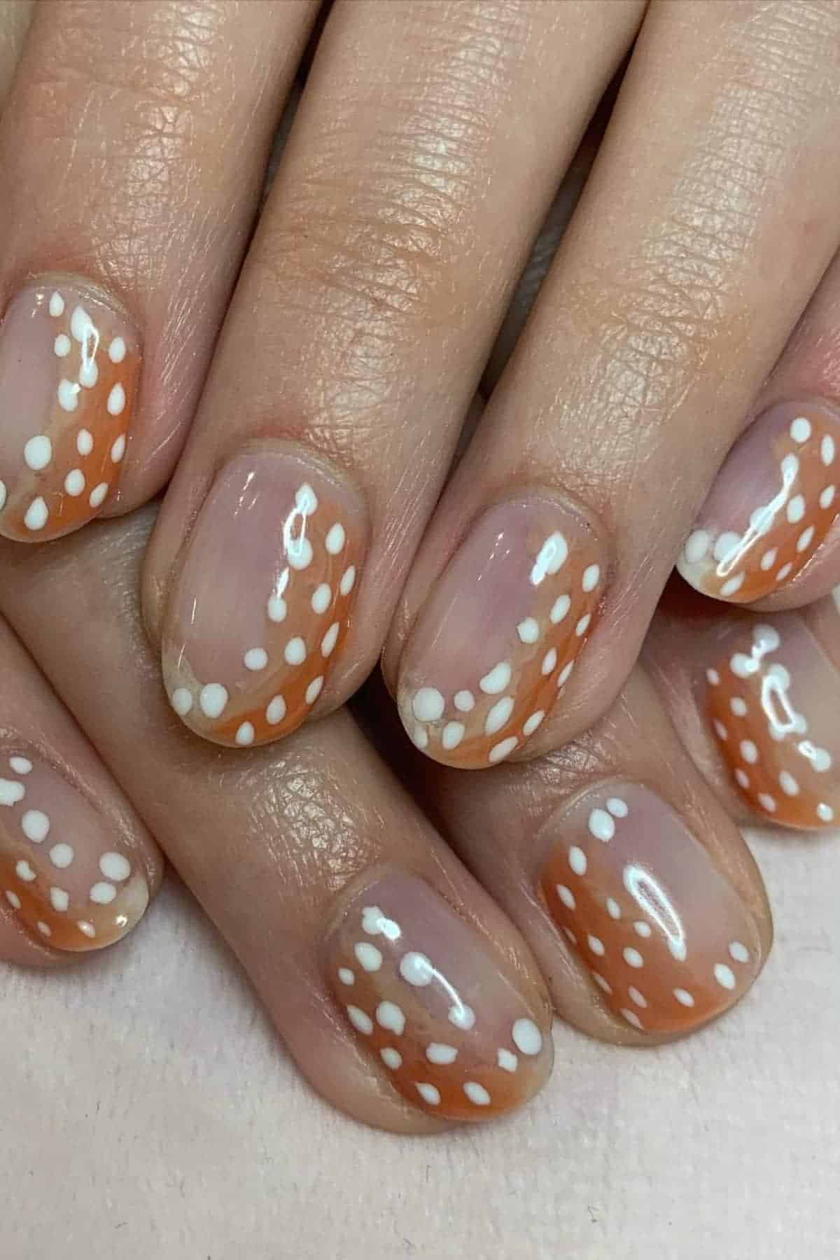 Fingernails with a translucent base, orange tips, and white polka dots arranged in curved lines along the tips.