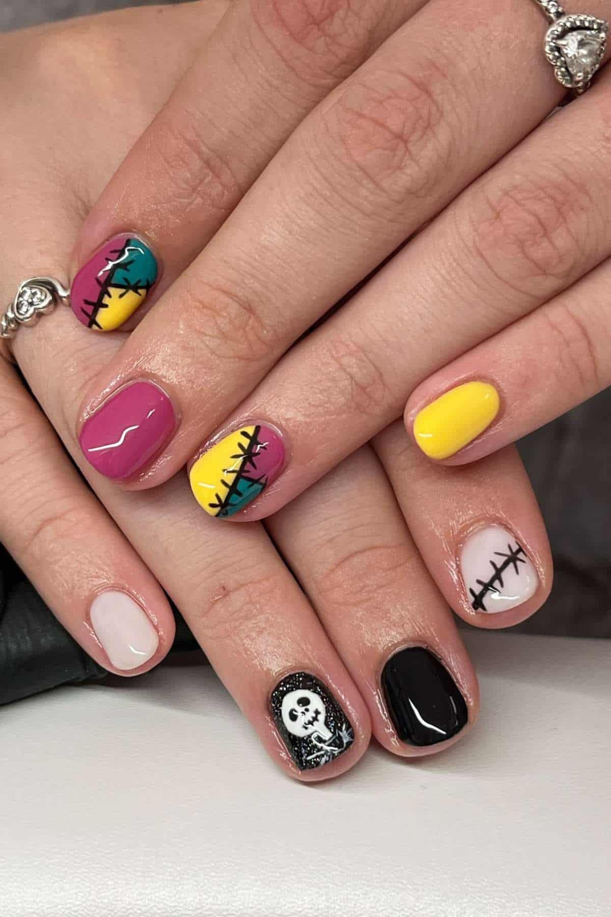 Hands with manicured nails featuring bright colors, stitched patterns, and a design of a black and white skull, inspired by "The Nightmare Before Christmas.