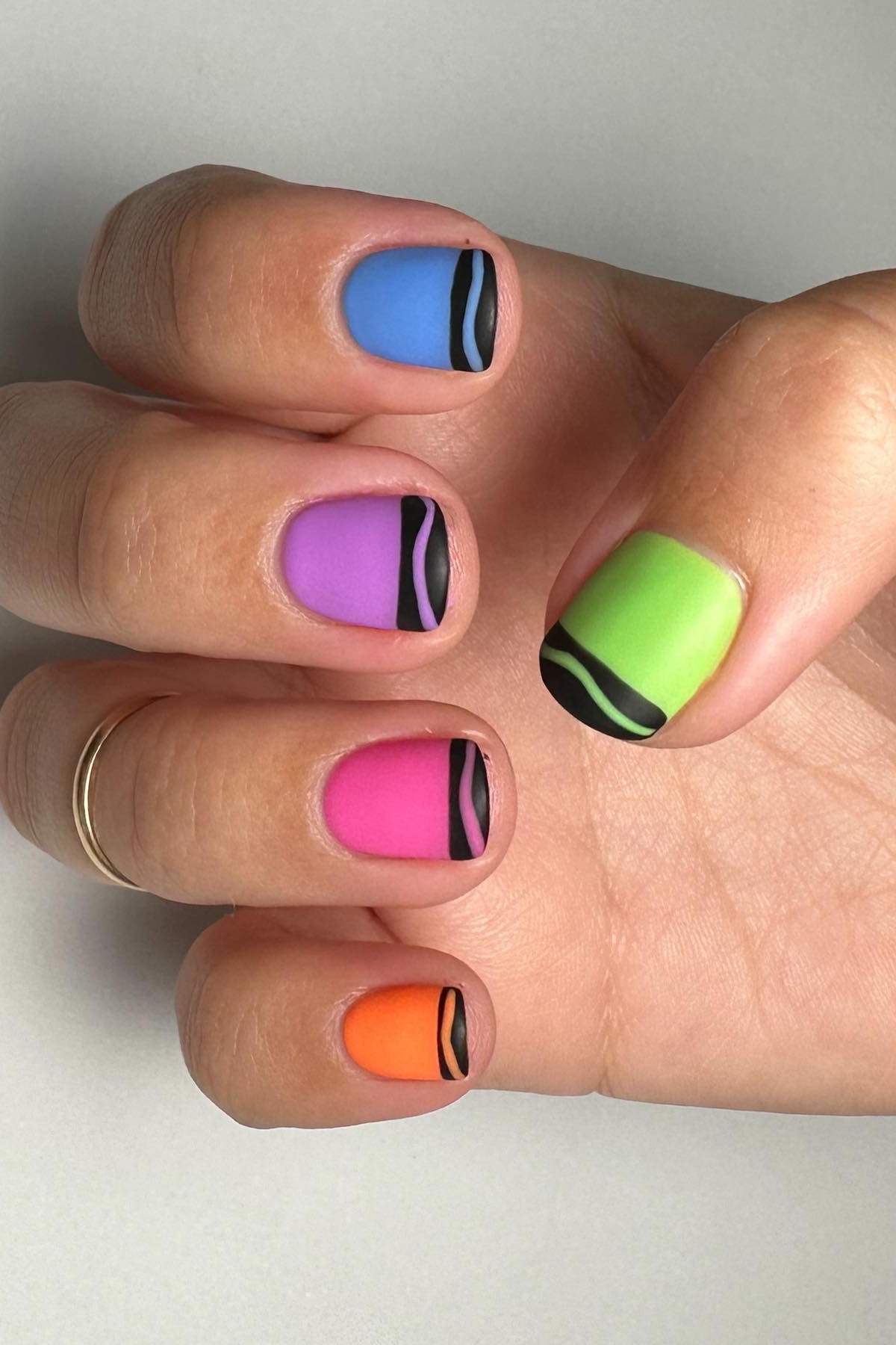 A hand with nails painted in bright colors—blue, purple, green, pink, and orange—each with a matte finish and a black wavy line near the tips.
