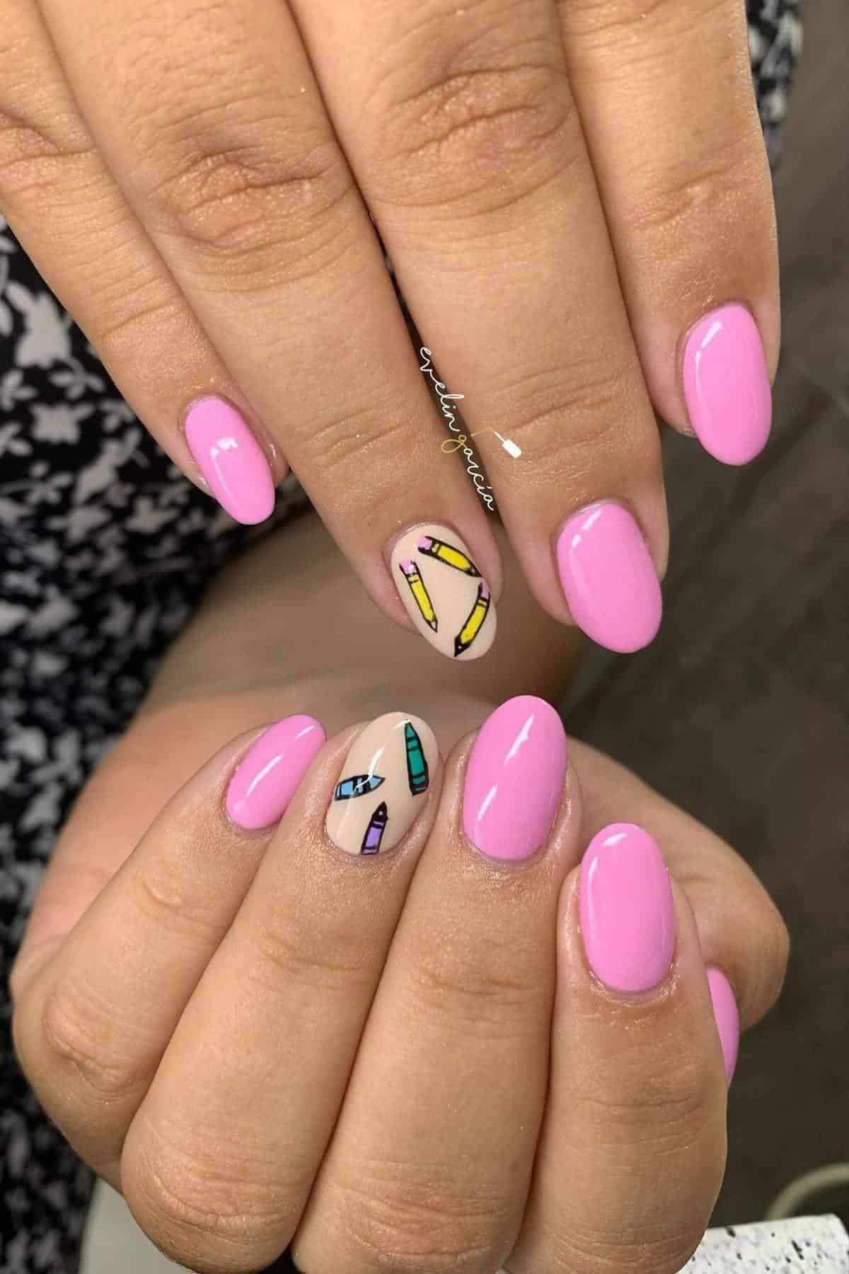 Hands with short, rounded nails painted light pink; two accent nails feature colorful crayon designs on a nude base.