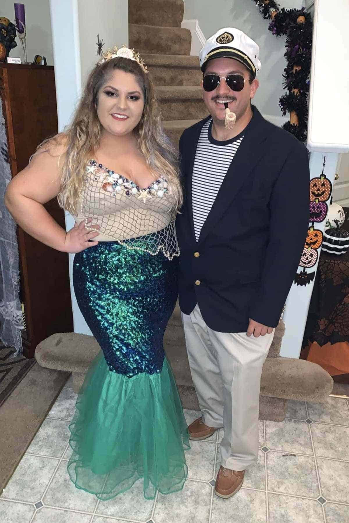 Two people in costumes: one dressed as a mermaid with a tiara and sequin tail, the other as a sailor with a captain's hat, sunglasses, and a fake pipe.