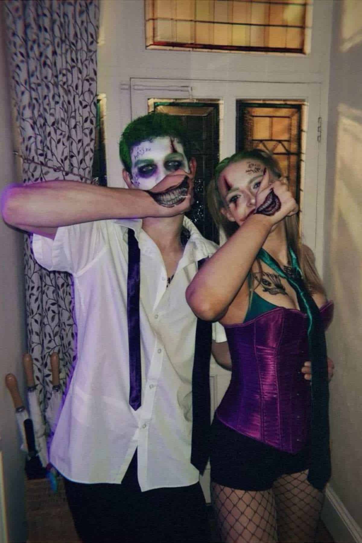 Two people in Joker-inspired costumes pose indoors, with painted faces and drawn-on smiles on their hands, holding them up to their mouths.