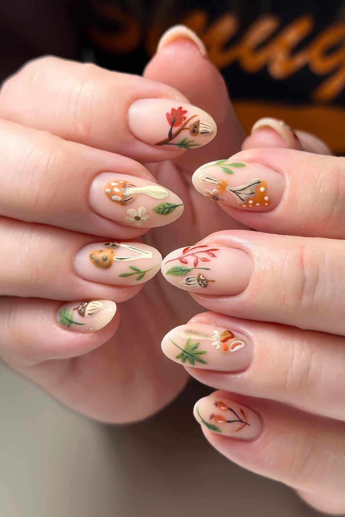 Close-up of hands with almond-shaped fingernails, each painted with delicate floral designs in earthy tones on a light nude base.
