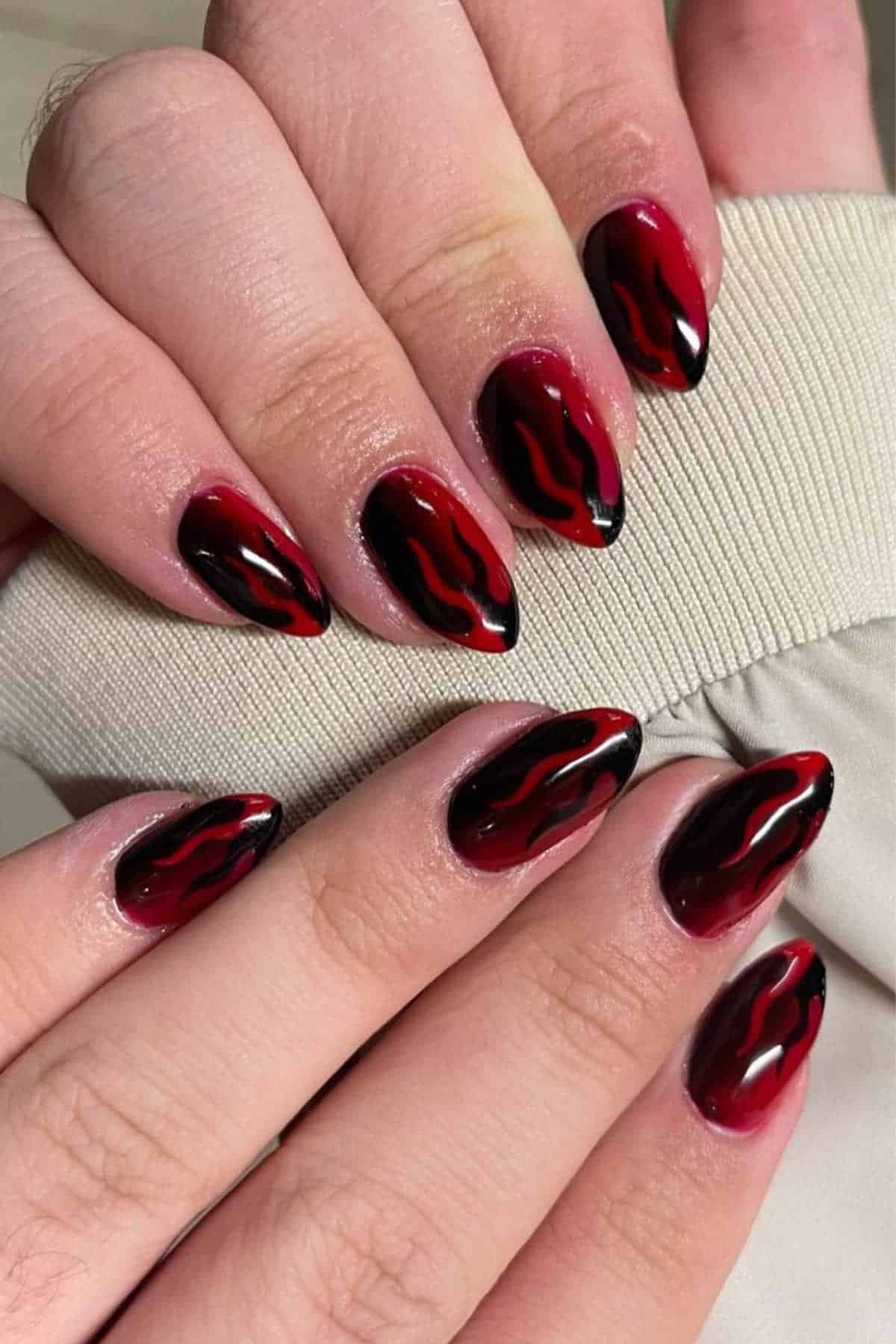 Close-up of hands with almond-shaped nails painted in a red and black flame design.