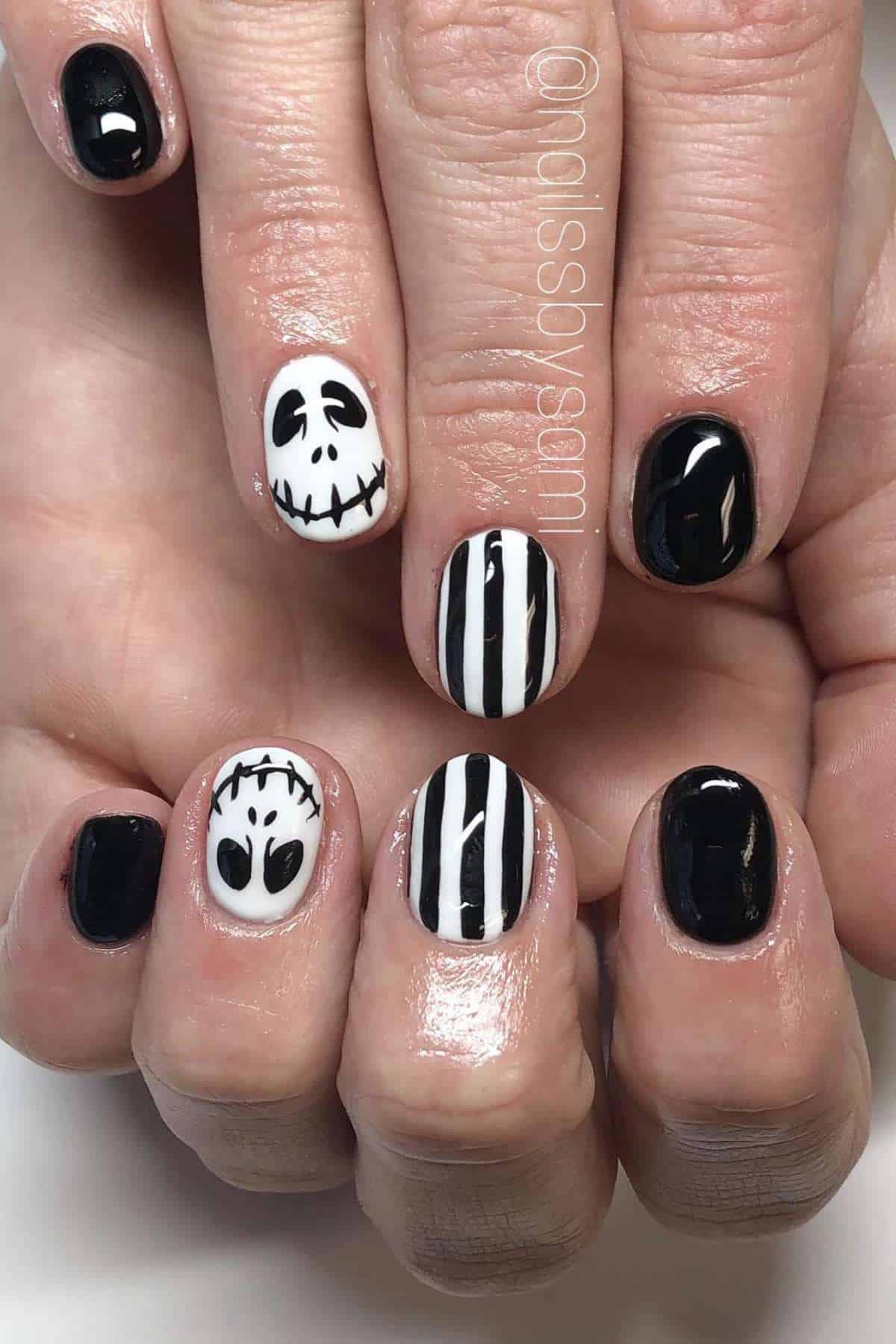 Close-up of hands with black and white nail art, featuring skulls, stripes, and solid black polish on short nails.