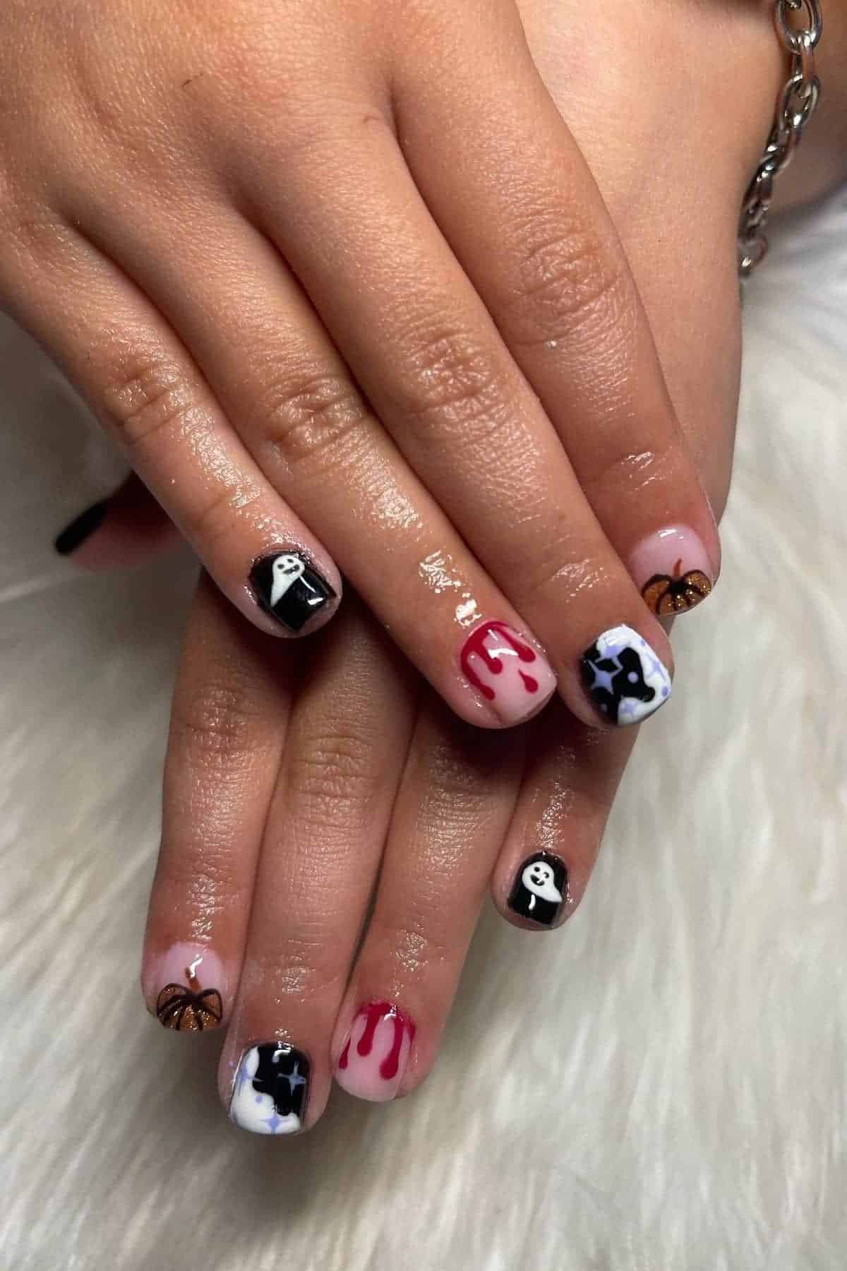 Hands with Halloween-themed nail art, including ghosts, bats, spider webs, dripping blood designs, and stars, shown on a white fur background.