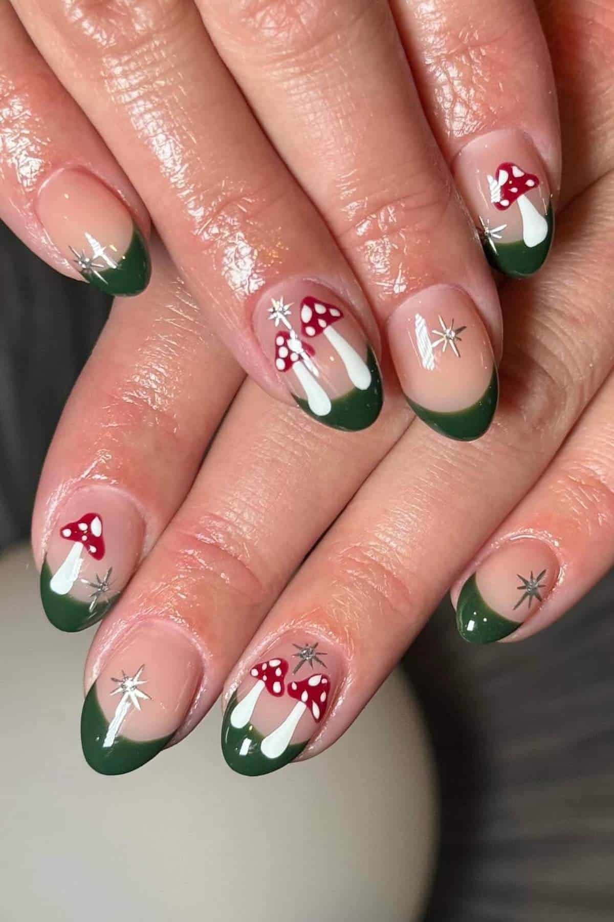 Close-up of hands with green French tip nails, red and white mushroom designs, and silver star accents on a neutral background.
