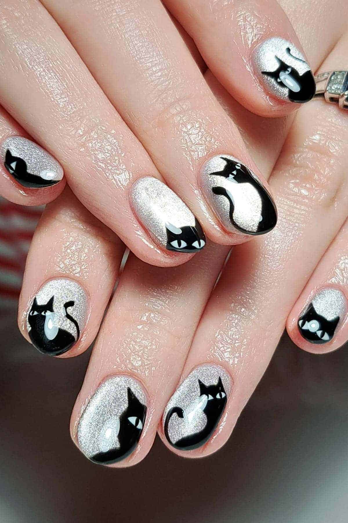 Fingernails painted with silver polish and black cat designs, each showing different cat poses and facial expressions.