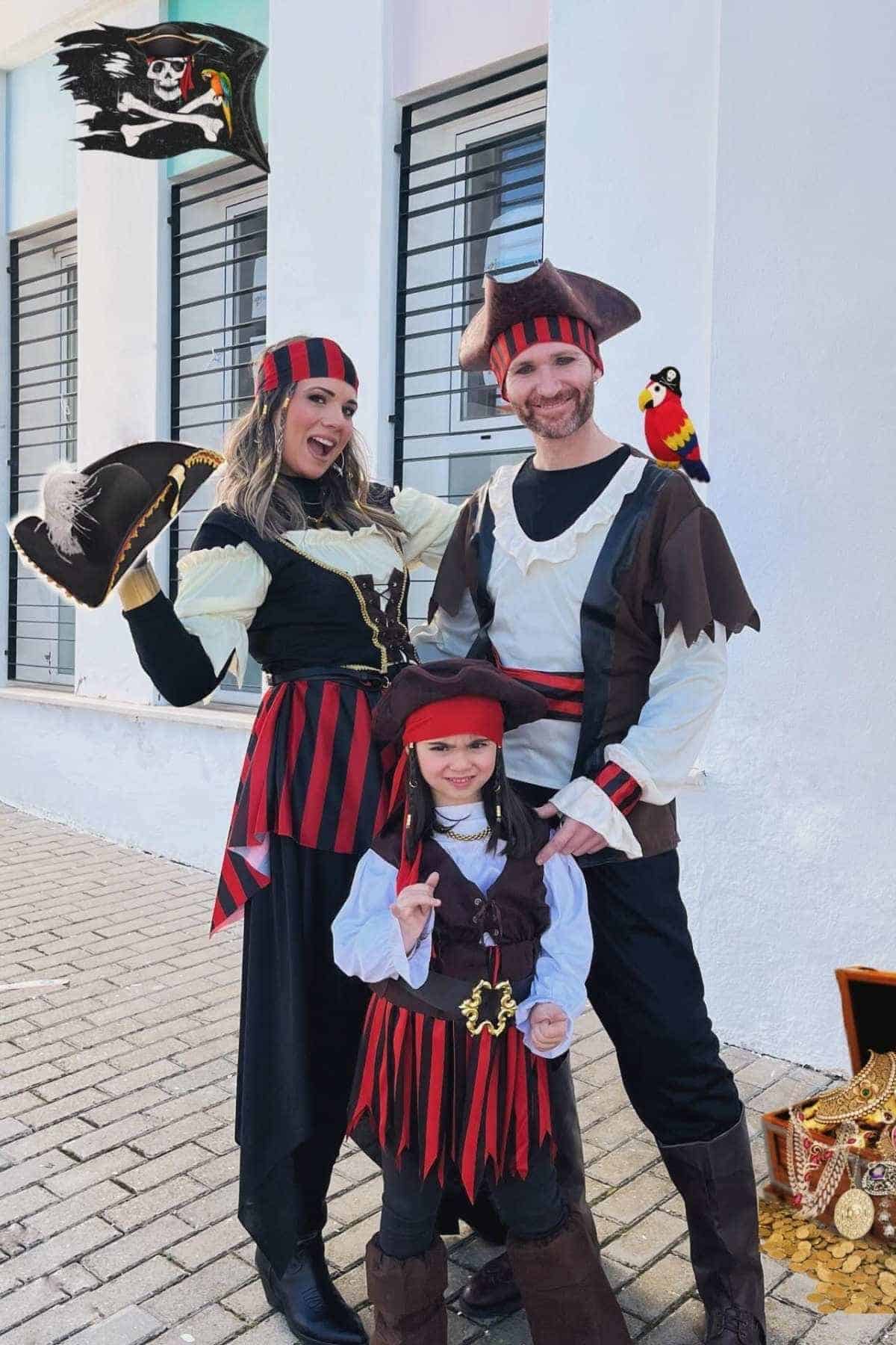 Three people dressed as pirates pose outside a white building, with a pirate flag, a parrot on a man’s shoulder, and a treasure chest filled with gold at their feet.