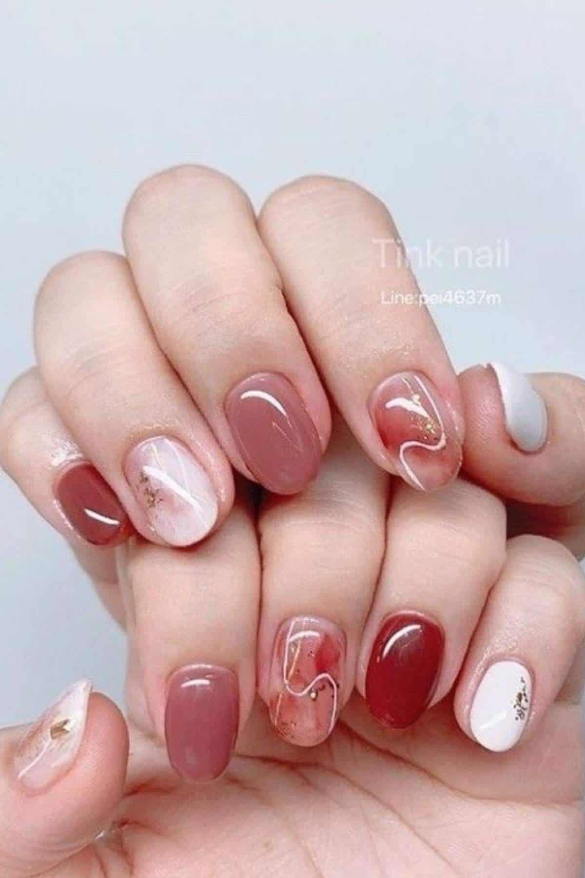 Hands with manicured nails in red, pink, white, and nude tones, featuring marble and gold accent designs on some nails.