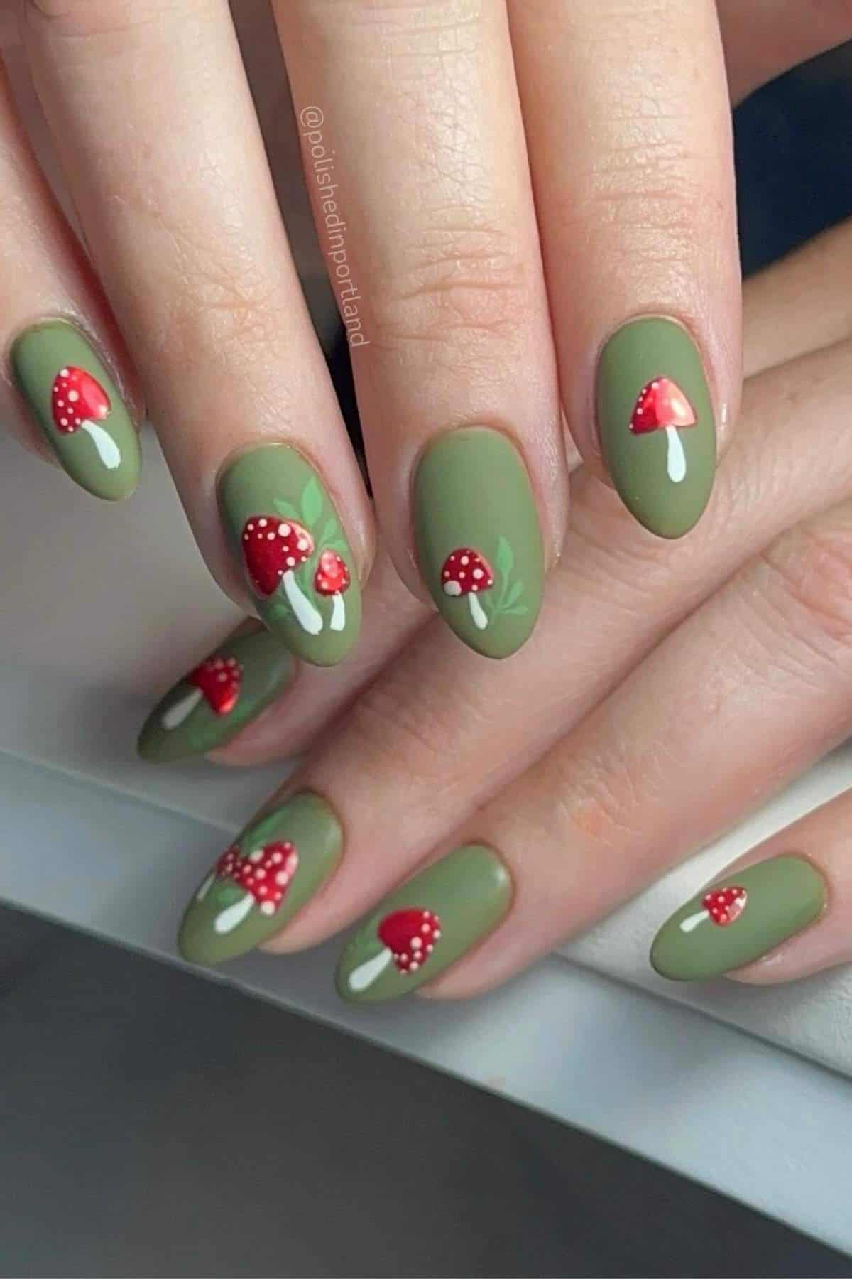 Hands with green matte nail polish, each nail featuring a small red and white mushroom design.