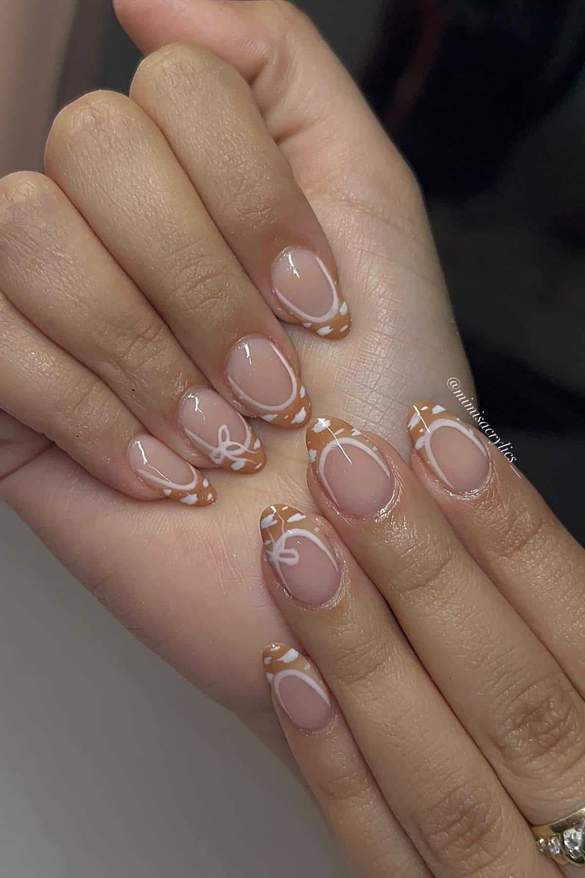 Hands with almond-shaped nails featuring brown and white abstract designs, including bows and French tip patterns, on a neutral base.