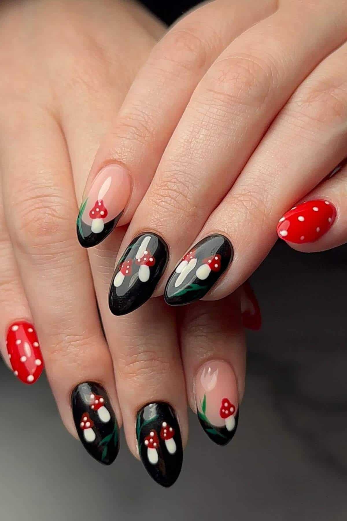 Hands with almond-shaped nails featuring red mushrooms with white spots on black, nude, and red backgrounds; some nails have white polka dots.