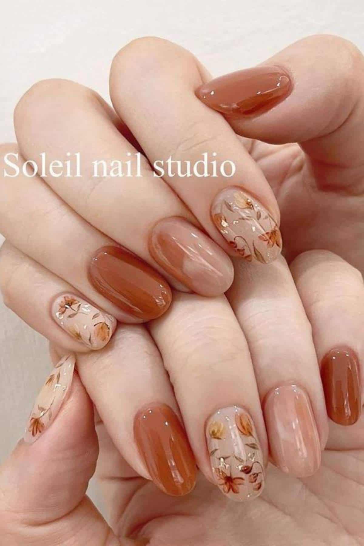 Hands with medium-length oval nails, painted in brown and nude tones, featuring floral designs on two accent nails. Text reads "Soleil nail studio.