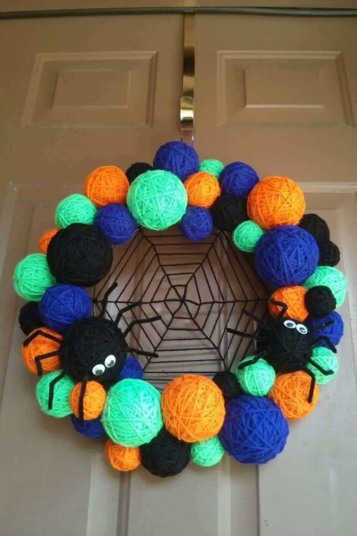 Yarn ball wreath in neon green, orange, blue, and black colors with black yarn spiders and a web, hanging on a door.