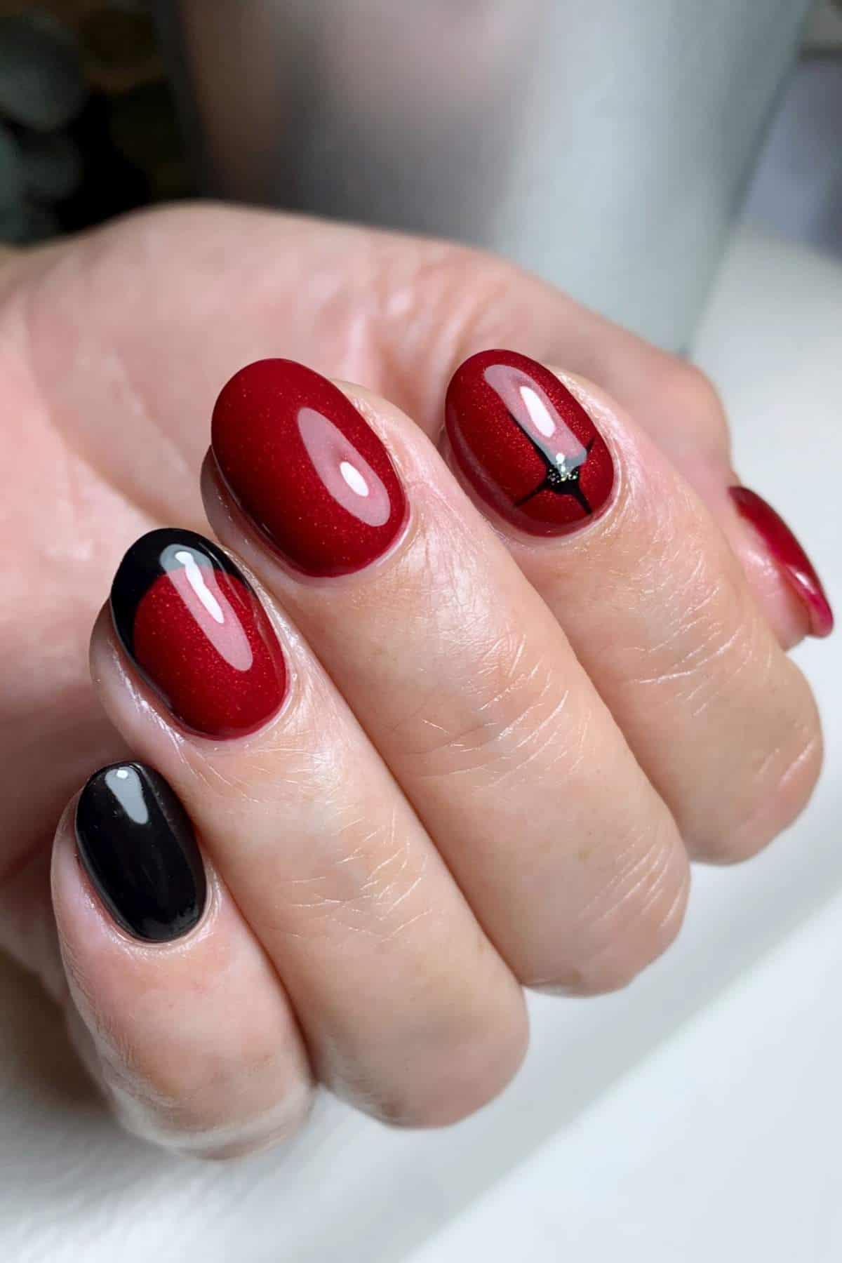 A hand with manicured nails painted in glossy red and black, with one nail featuring a thin black line and star design on a red background.