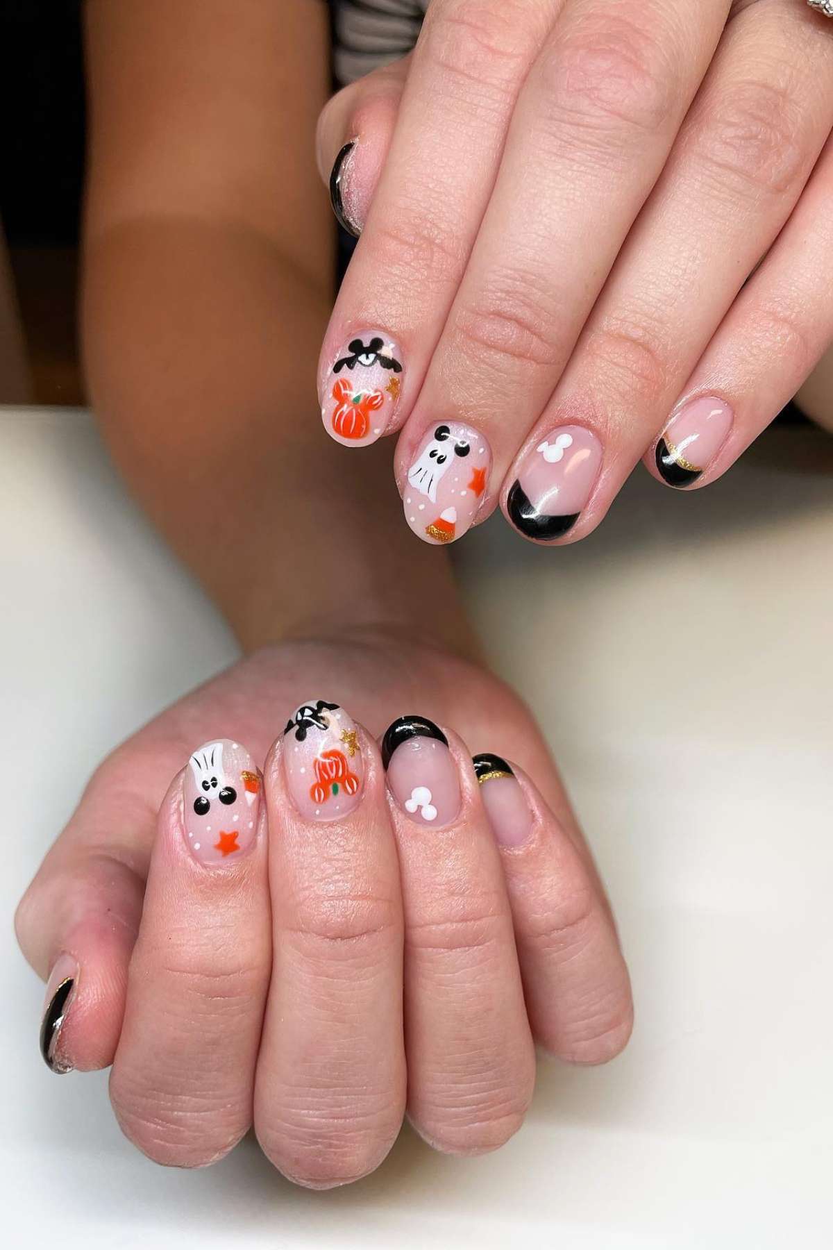 Hands with manicured nails featuring Halloween-themed designs, such as ghosts, pumpkins, and bats, along with black tips and small white accents.