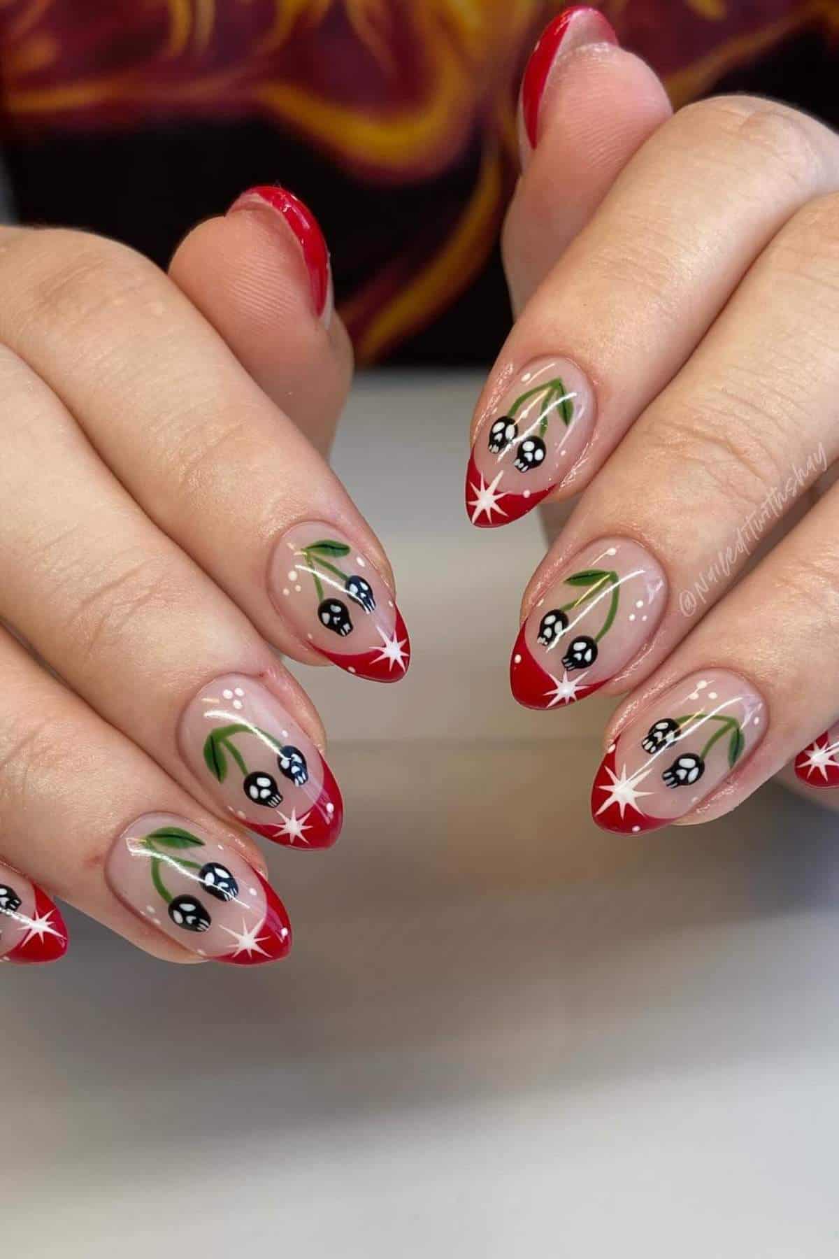 Hands with almond-shaped nails featuring red French tips, white stars, and black and white floral designs with green leaves on a nude base.
