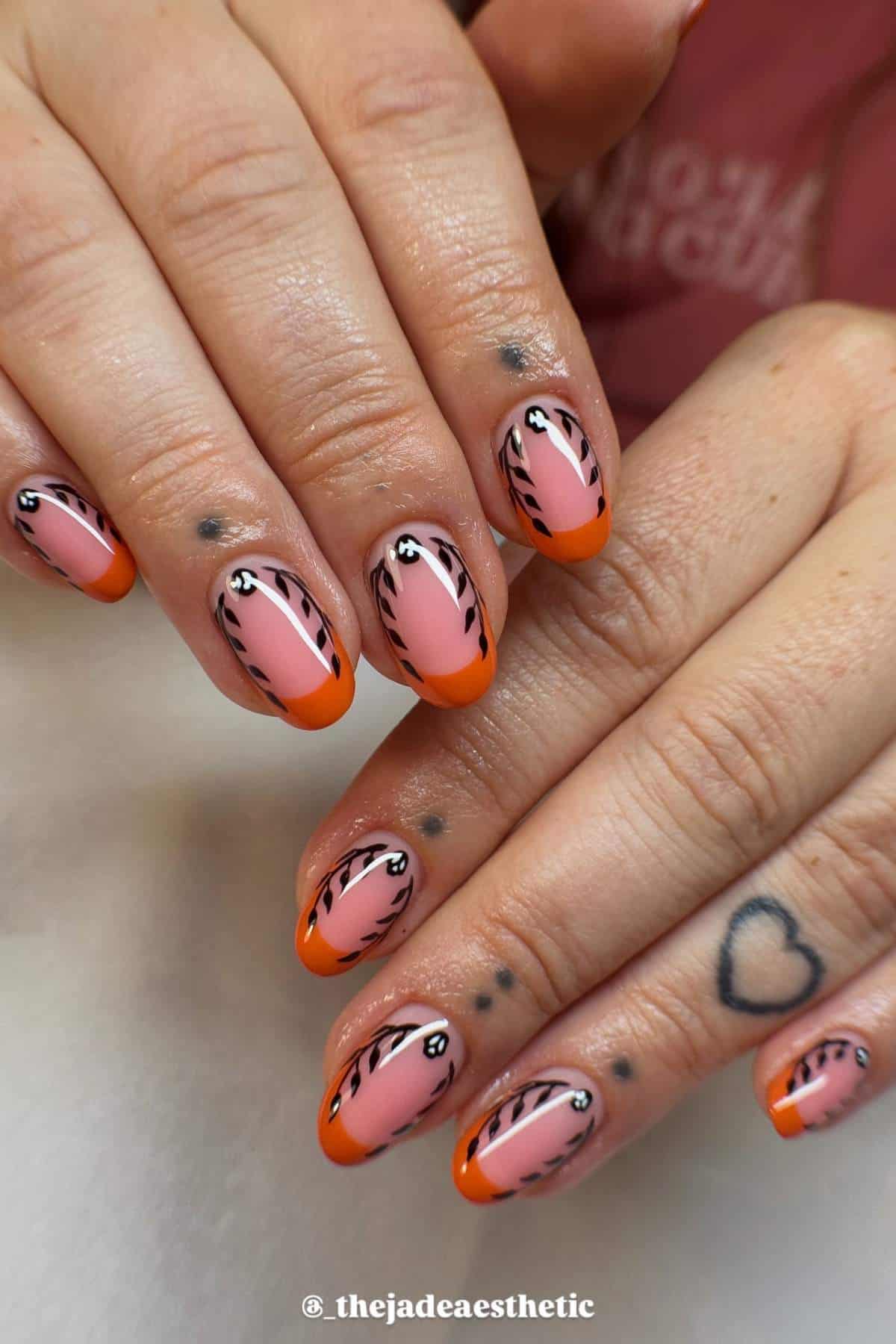 Hands with pink and orange French tip nails featuring black and white tiger stripe designs; heart and dot tattoos visible on fingers.