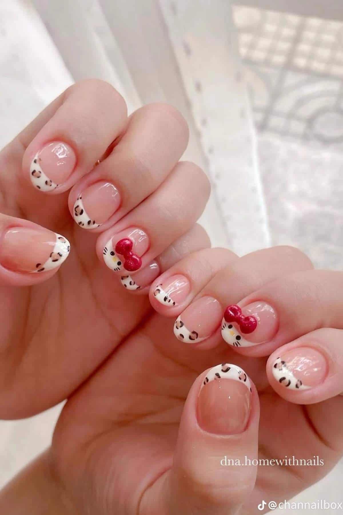 Hands with manicured nails featuring white French tips with black spots and two accent nails with red bows and Hello Kitty faces.