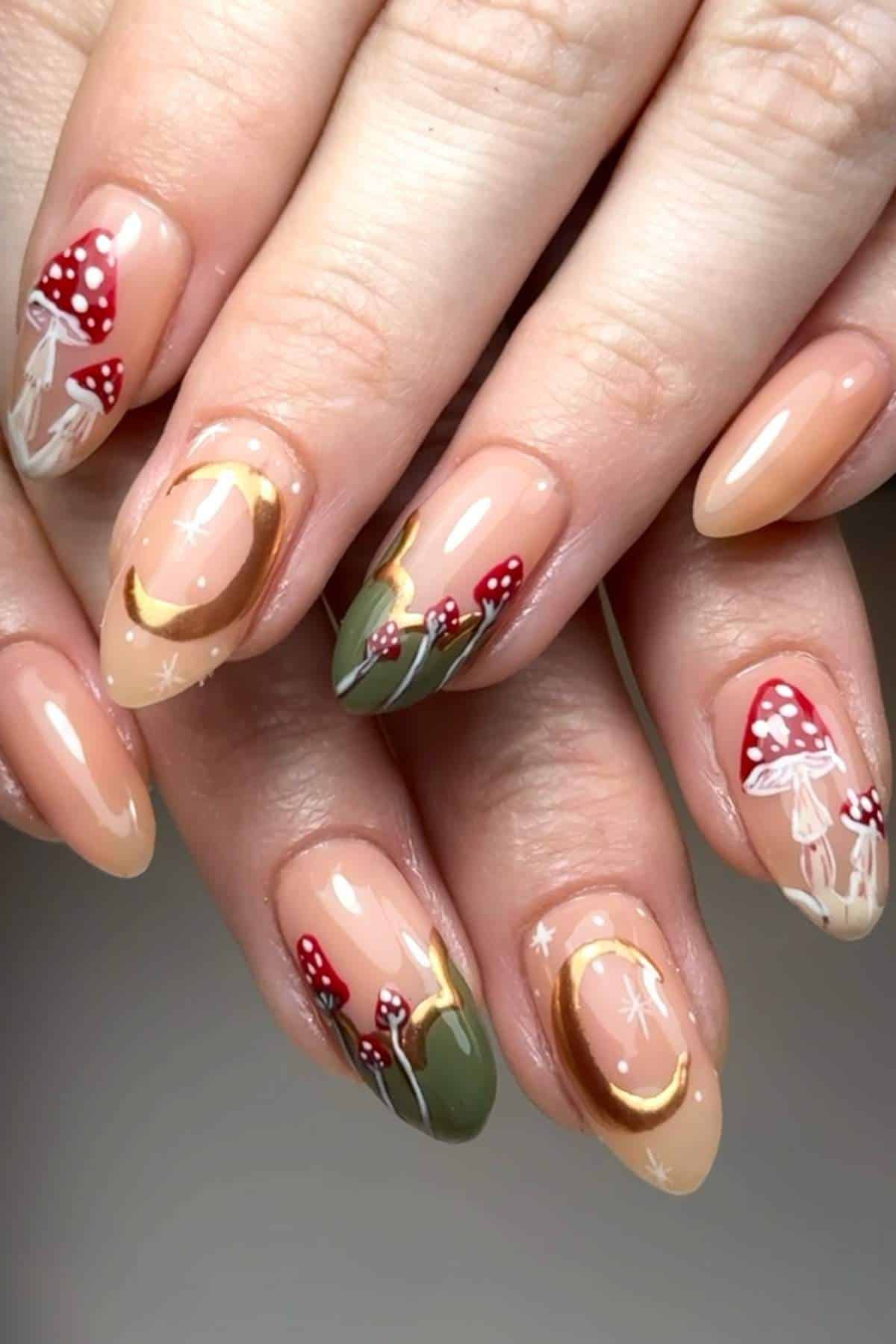 A hand with long almond-shaped nails, painted with mushrooms, greenery, gold accents, and jellyfish designs on a nude base.