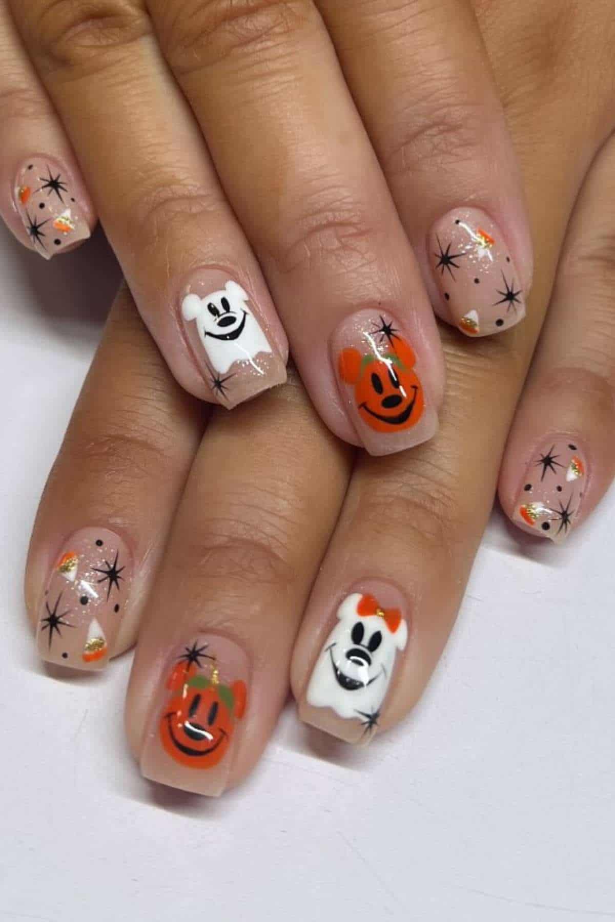 Fingernails with clear polish feature black starbursts, candy corn designs, and cartoon bear faces in white and orange on a neutral background.