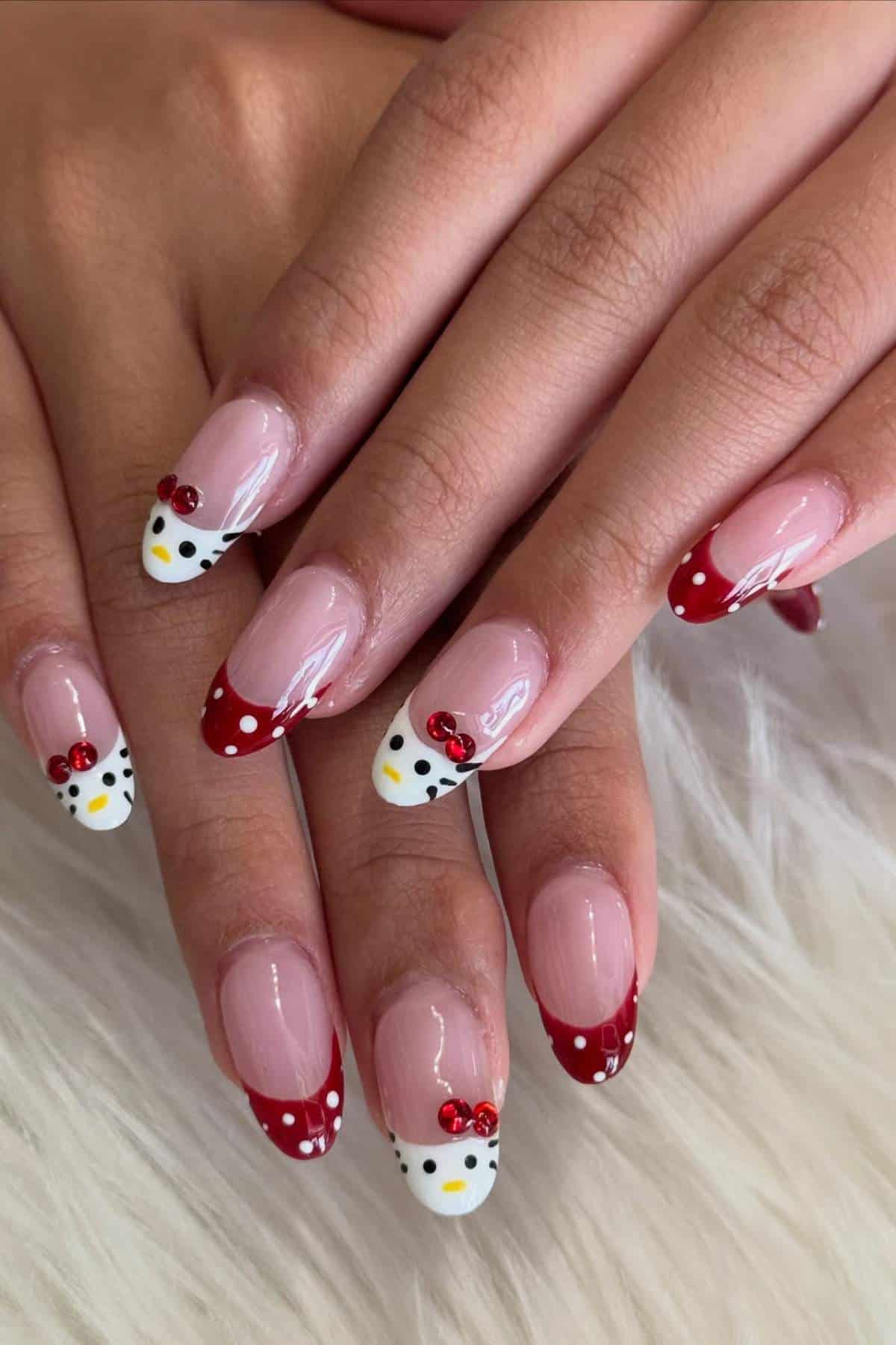 Hands with long nails featuring red French tips, white polka dots, and Hello Kitty face designs on the tips. Nails rest on a white, fluffy surface.