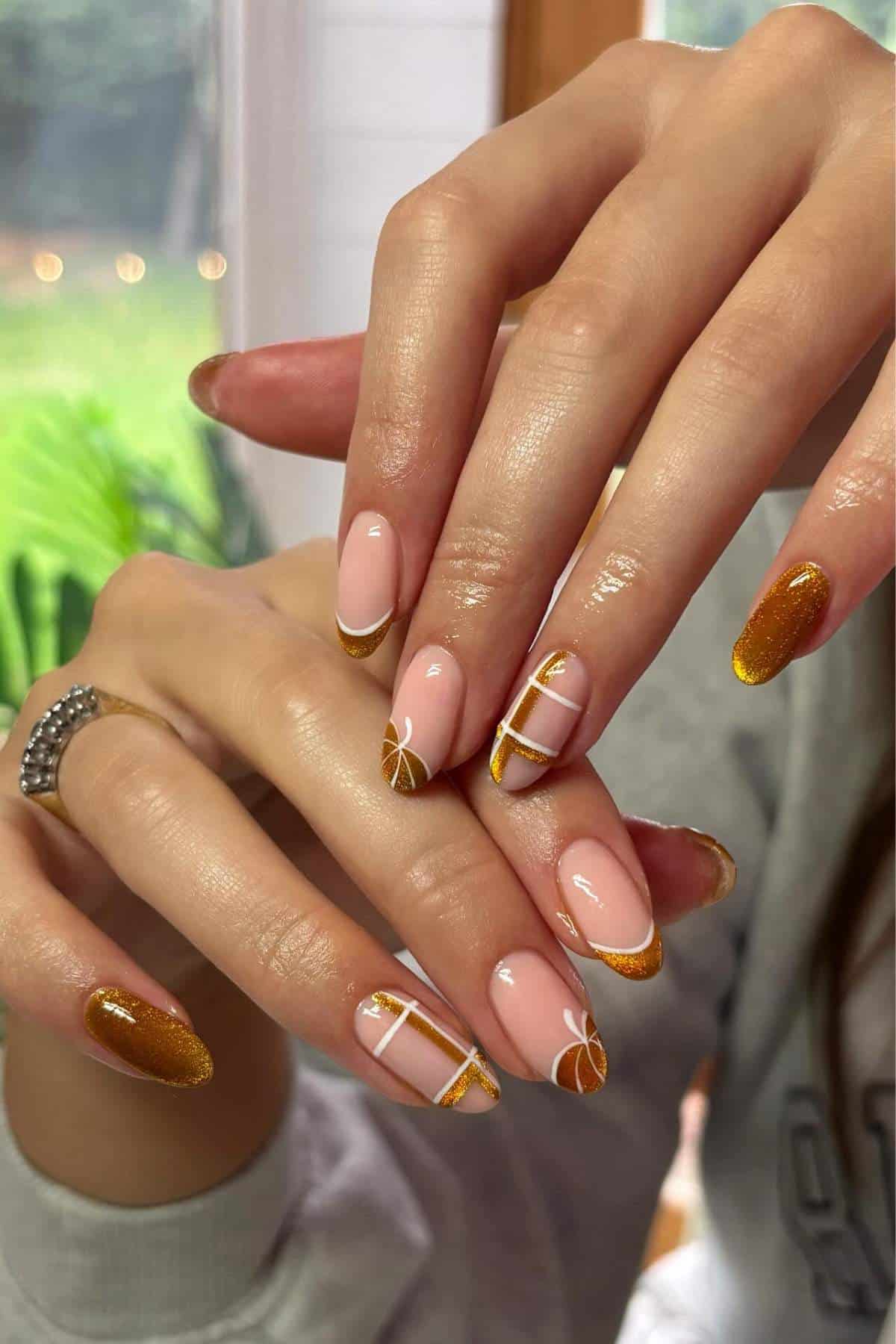 Close-up of hands with manicured nails featuring orange, gold, and nude colors, decorated with geometric lines and citrus slice designs.